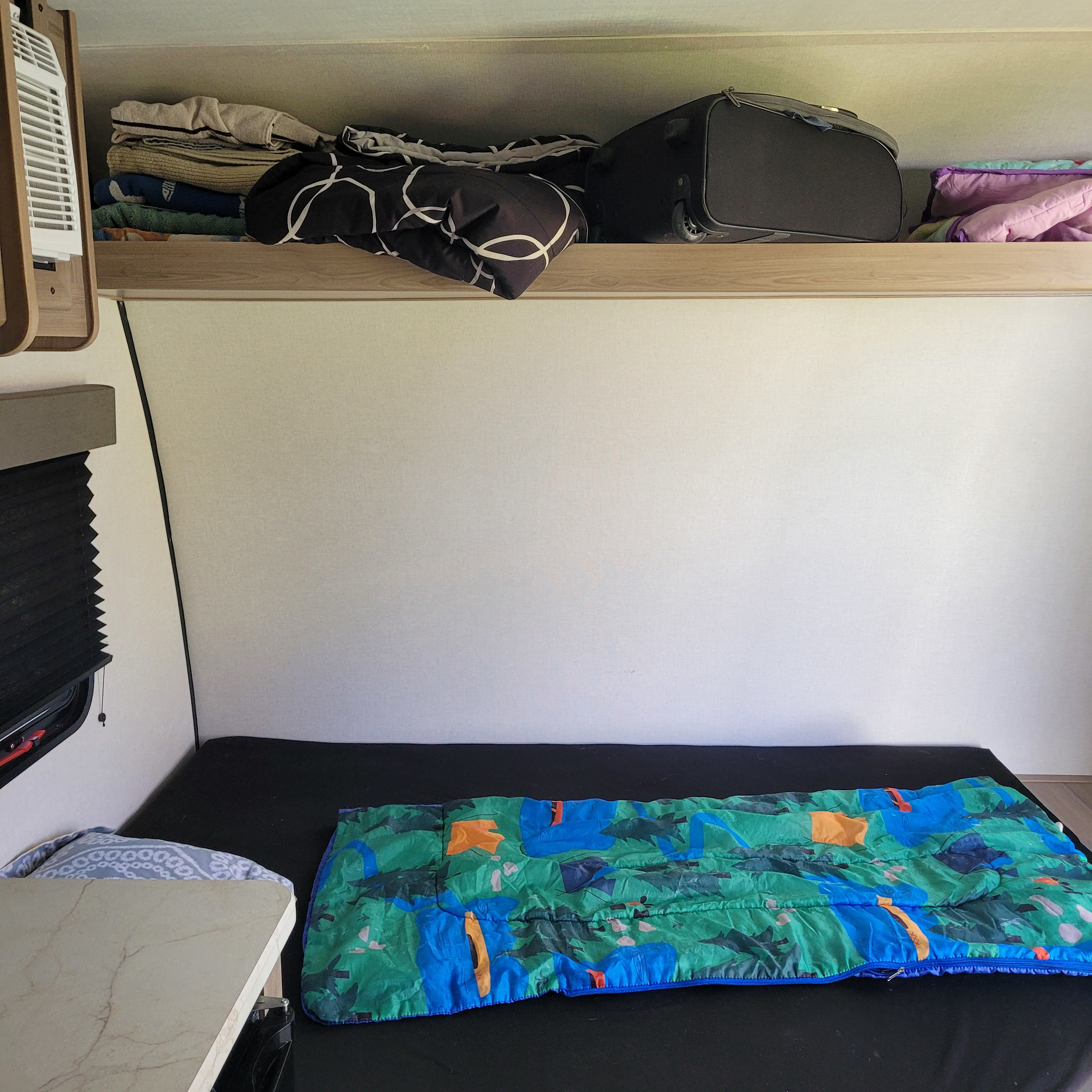 Cozy rv rental sleeping area with a colorful sleeping bag, overhead luggage, linen storage, and a small table.. 4YDTCME14TM937831 13B 2026