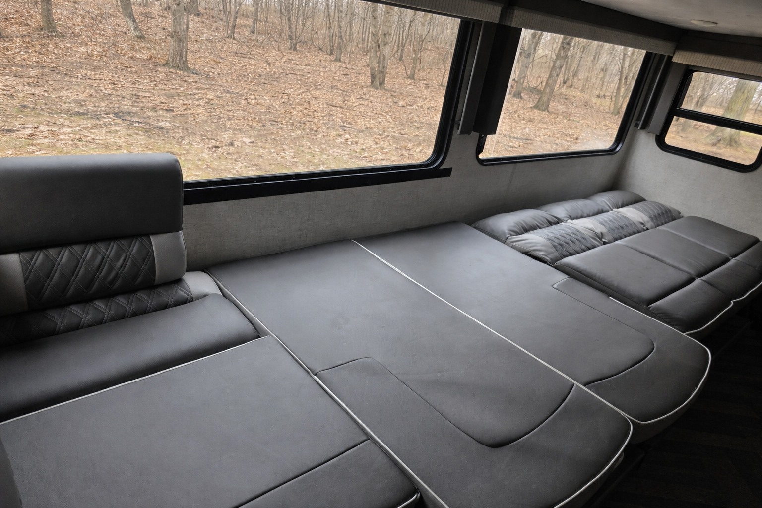 This RV rental showcases a convertible gray seating and bed area with large windows facing a wooded landscape.. Forest River Salem Cruise Lite 2021