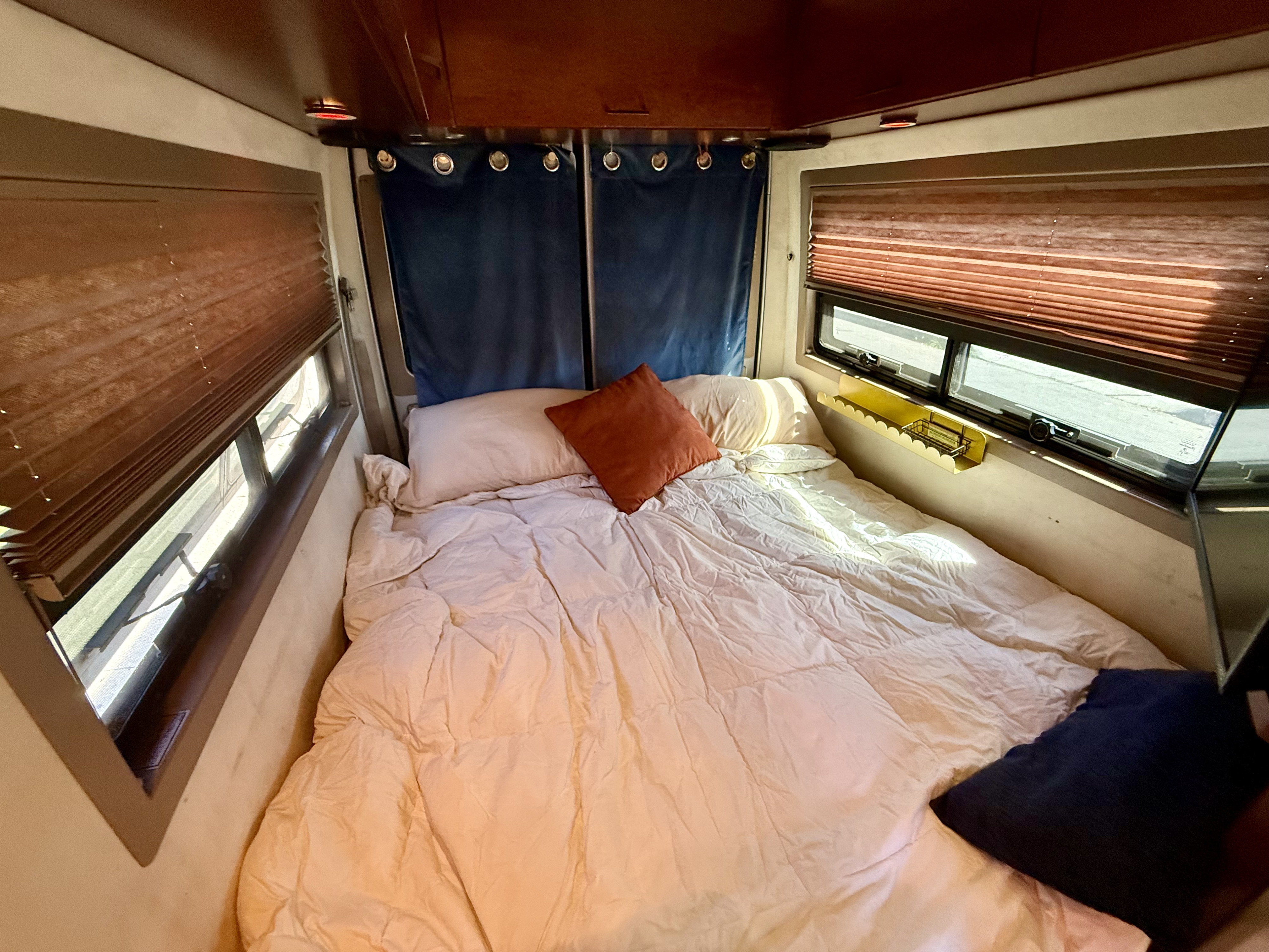 Experience comfort in this rv rental bedroom featuring a bed, warm comforter, pillows, side windows with blinds, and privacy curtains.. Pleasure-Way Pleasure-Way Class B 2006