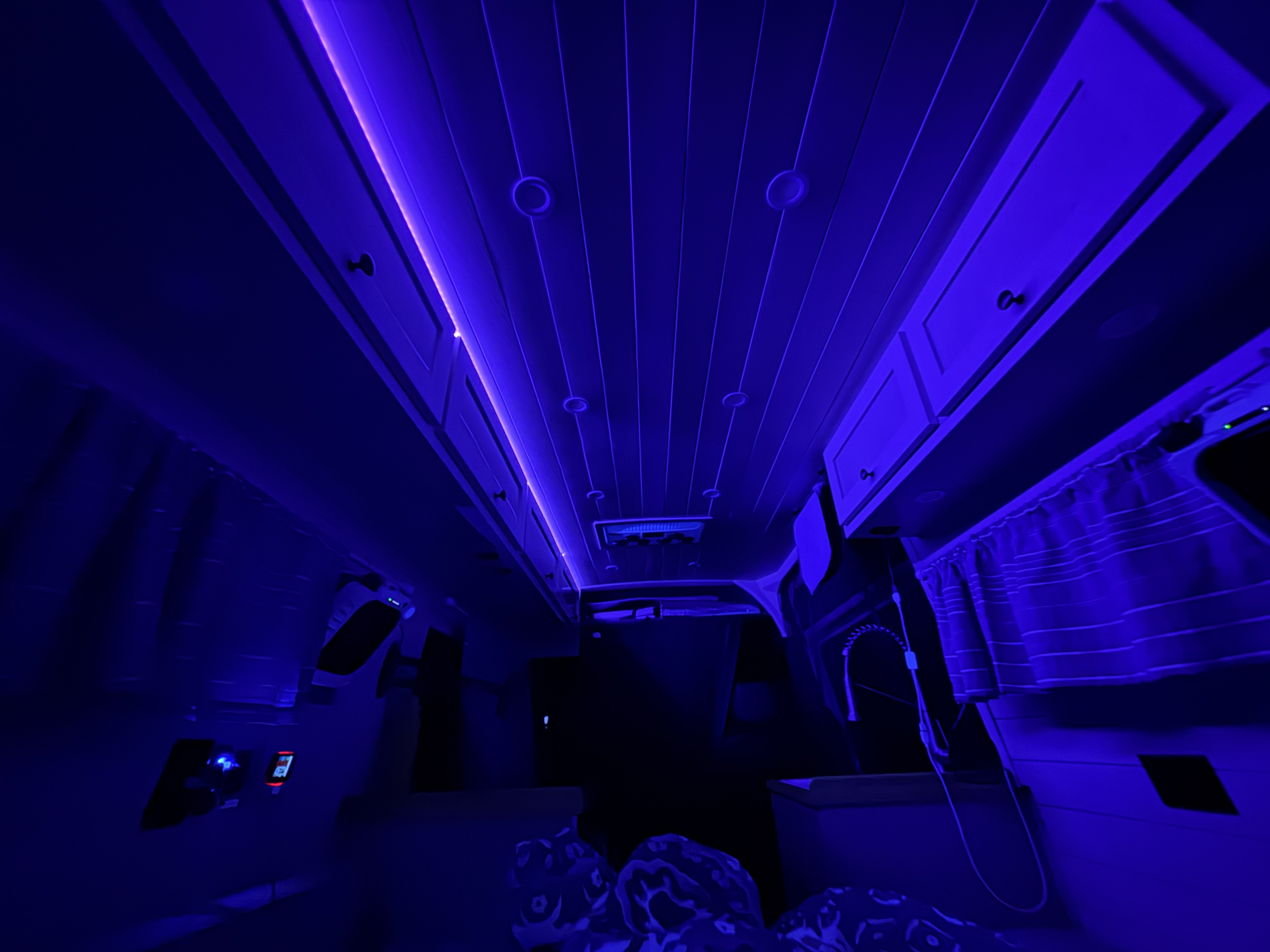 Dark blue-lit interior of an RV rental with overhead cabinets, slatted ceiling, and control panels for a modern campervan experience.. Mercedes-Benz Sprinter 2020