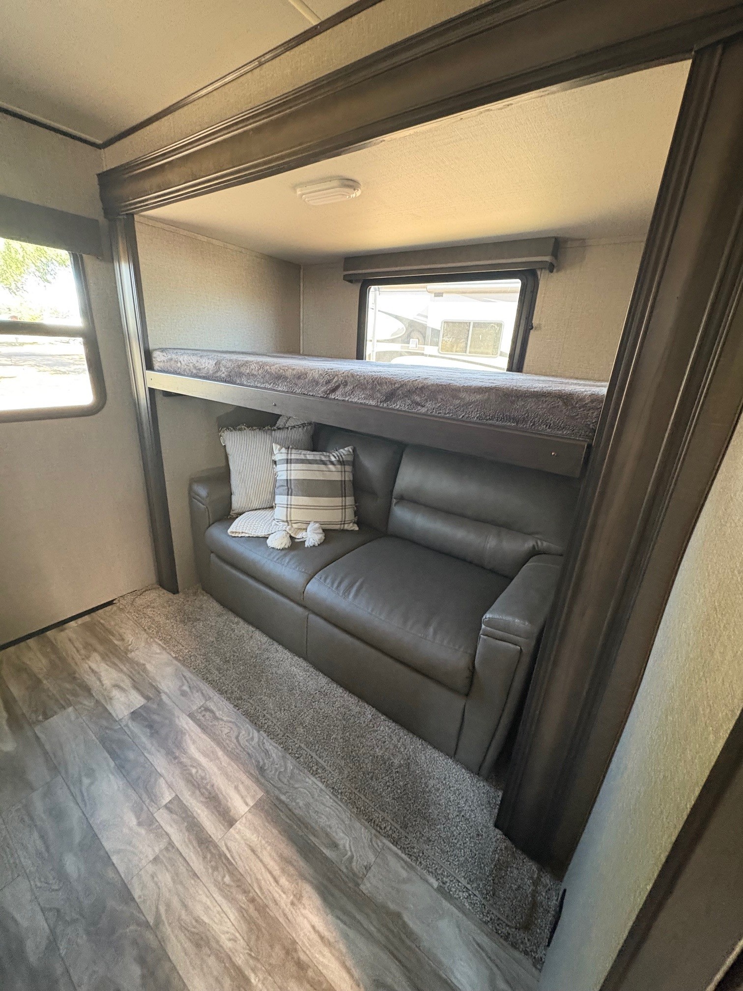RV rental bunk room: comfy grey sofa with pillows under a cozy bunk bed, wood flooring, and windows.. Grand Design Reflection 2021