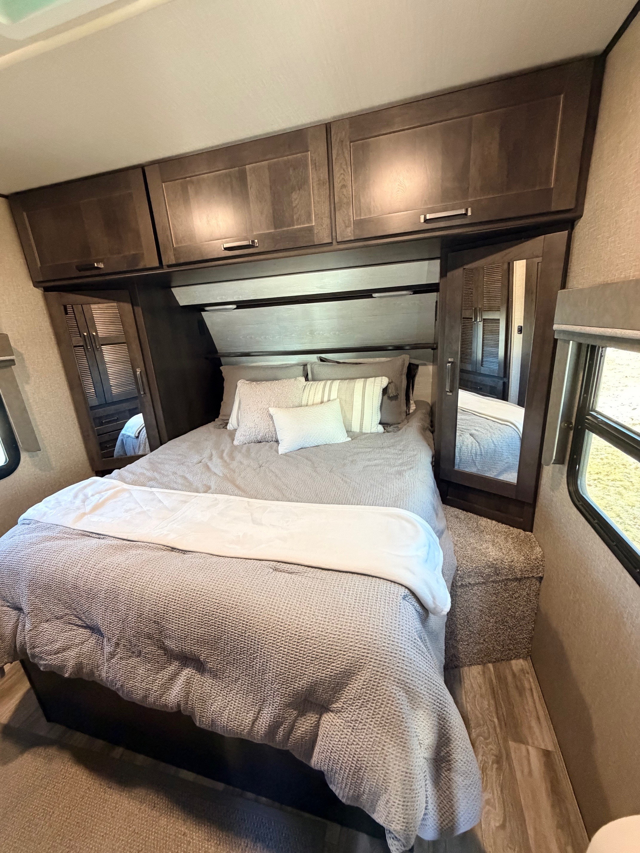 This cozy RV rental bedroom features a spacious bed, mirrored wardrobes, and overhead storage, ideal for travel accommodation.. Grand Design Reflection 2021