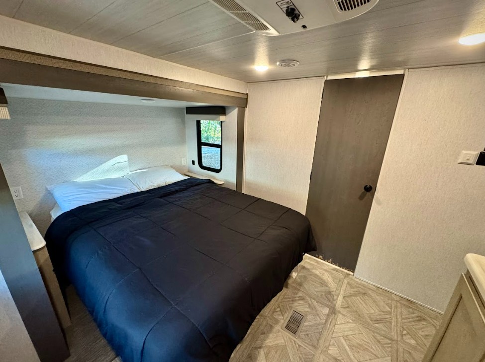 RV rental bedroom interior featuring a queen bed with dark comforter, overhead storage, a window, and patterned flooring.. Salem 36VBDS 2024