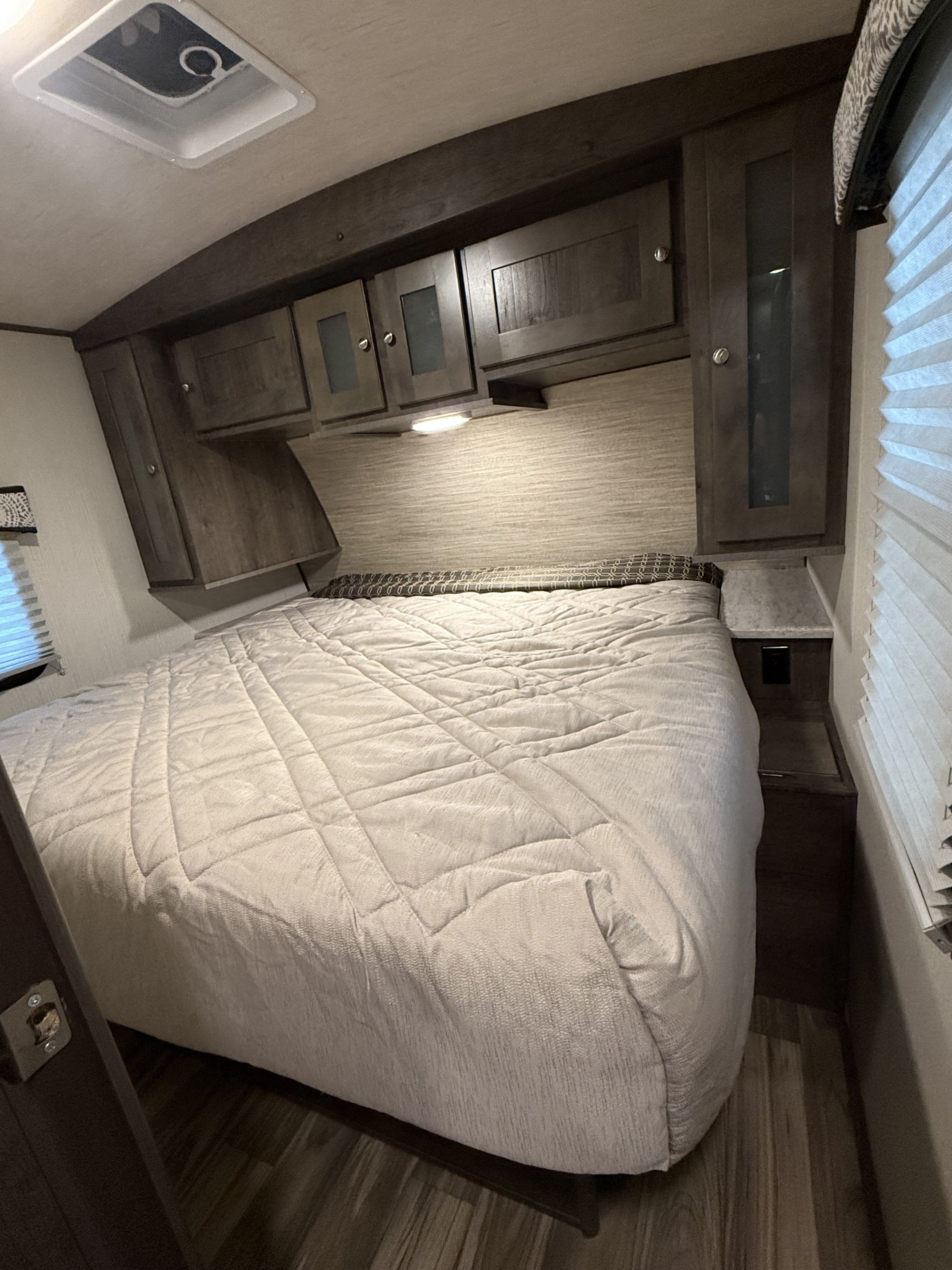 Cozy RV rental bedroom with a large quilted bed, dark wood overhead cabinets, and a ceiling vent. Ideal for comfortable travel.. Cruiser RV MPG Ultra Lite 2019