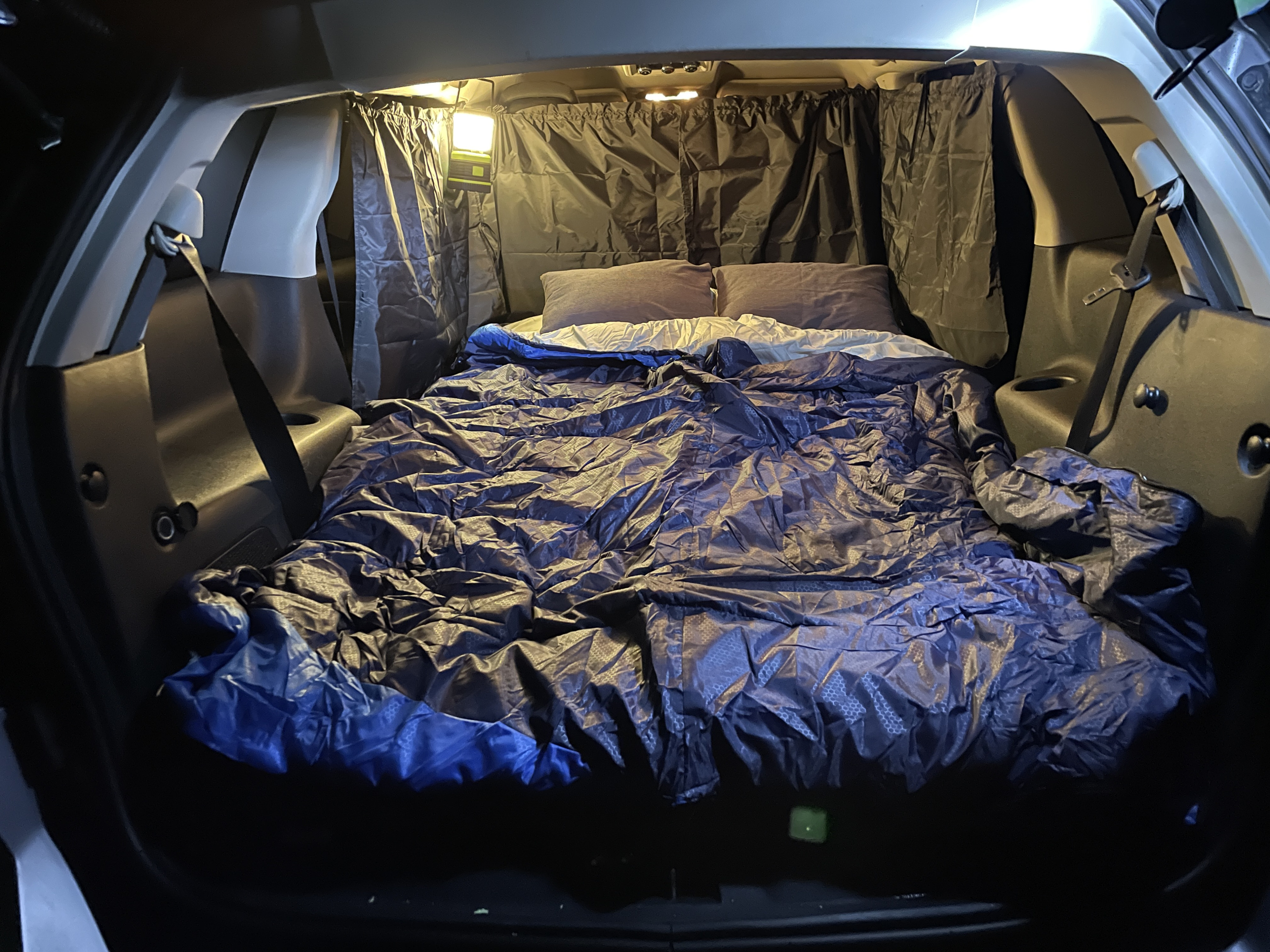 Cozy car camping setup with a comfortable bed, privacy curtains, and a lantern, ideal for an overnight stay or an affordable RV rental alternative.. Dodge Journey 2017