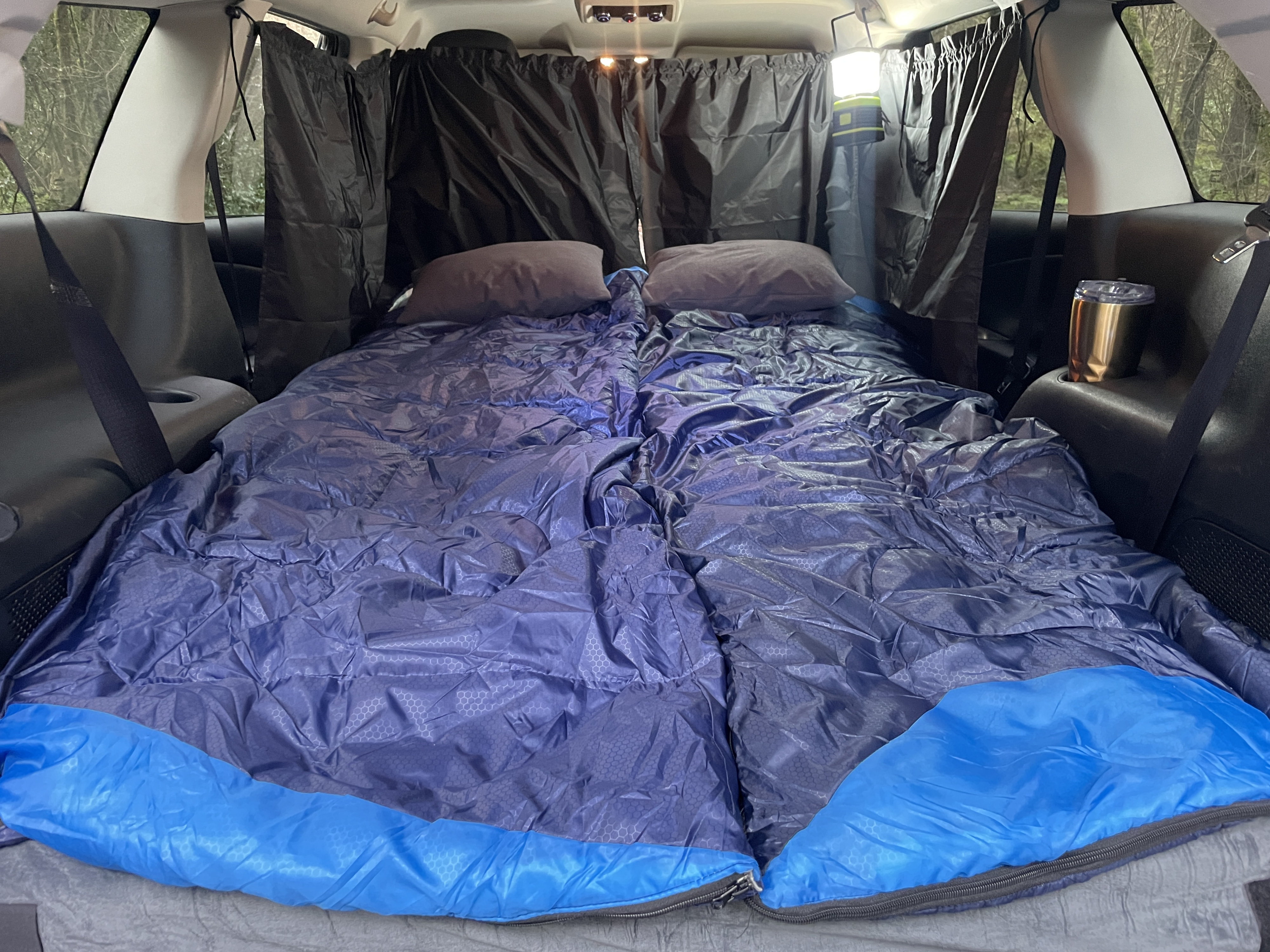 Cozy RV rental car camping setup with two blue sleeping bags, pillows, and privacy curtains for comfortable travel.. Dodge Journey 2017