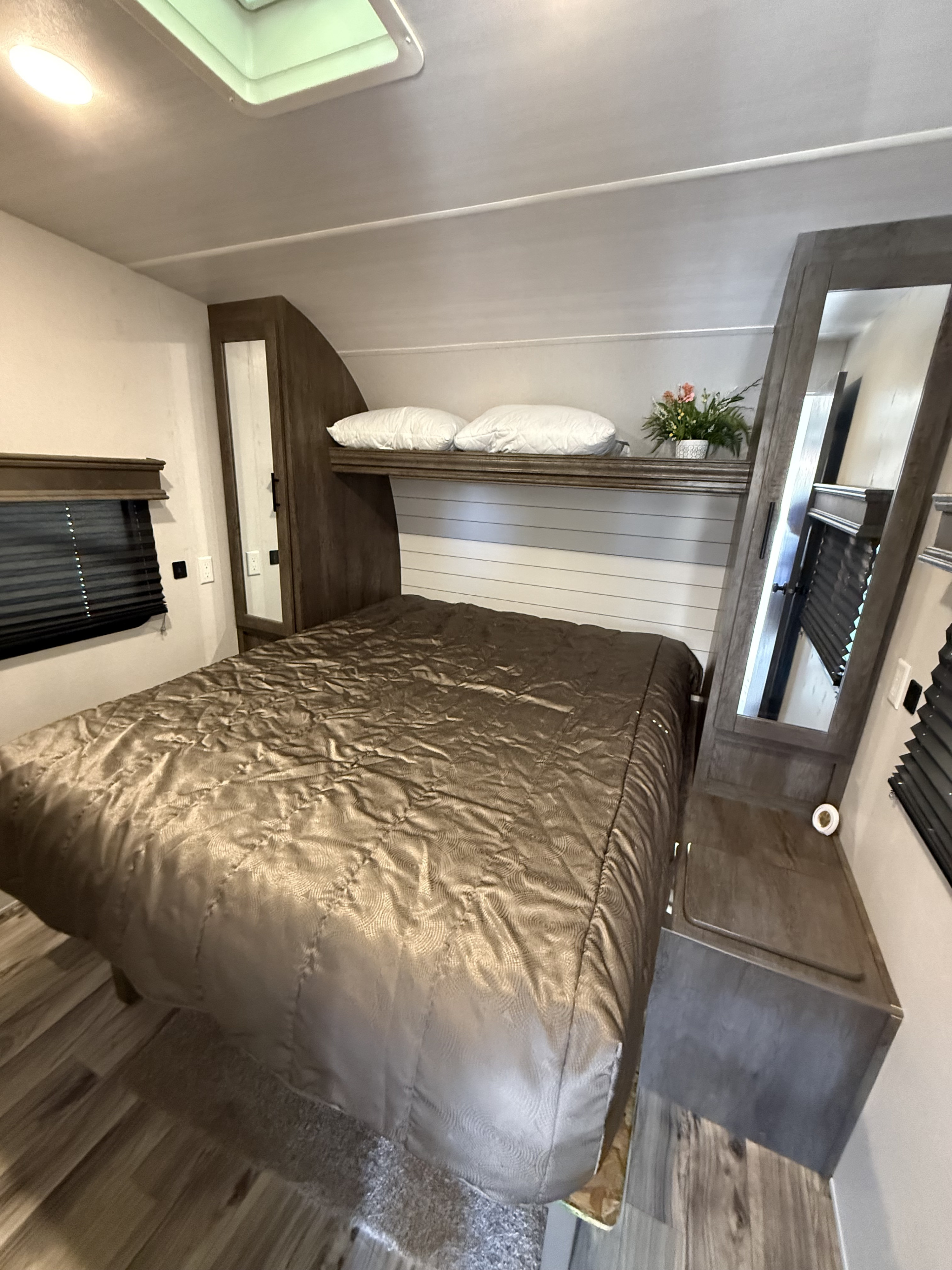 Comfortable RV rental bedroom featuring a queen bed, mirrored closets, a decorative shelf, and skylight.. Forest River Sandstorm 2020