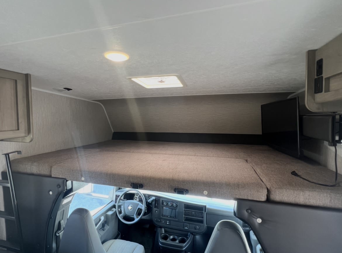 RV rental interior showing the large cab-over bunk bed with TV, ladder access, and the vehicle's cockpit below.. Coachmen Freelander 2021