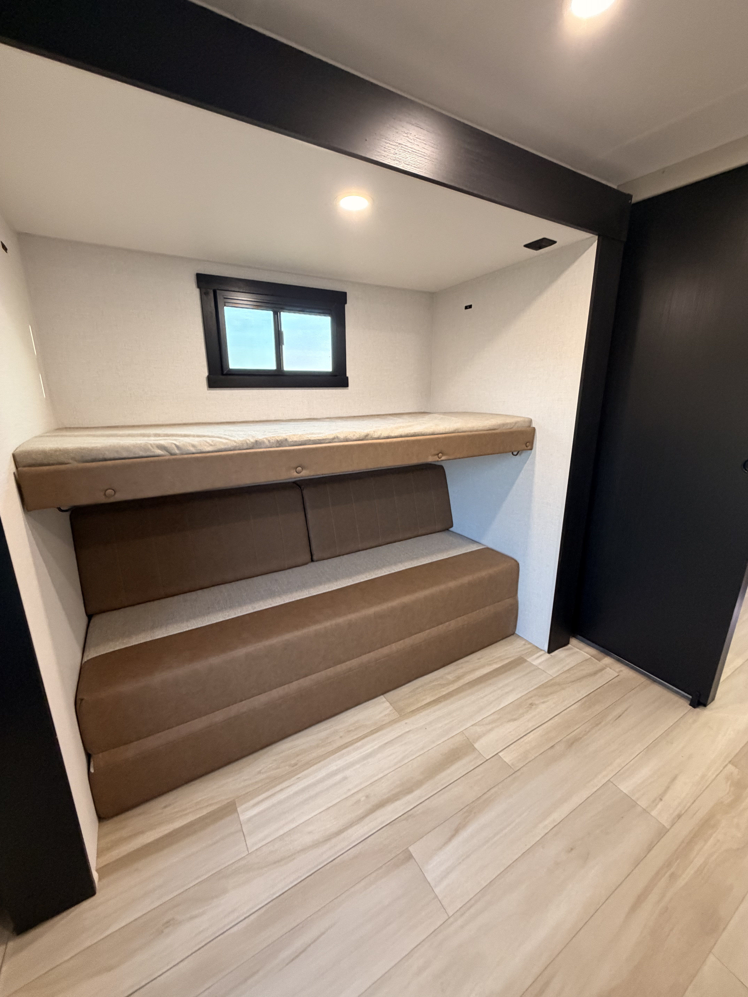 Modern RV rental bedroom/lounge: features an upper bunk bed over a convertible brown sofa, window, and light wood floor.. Forest River Salem Hemisphere 2026