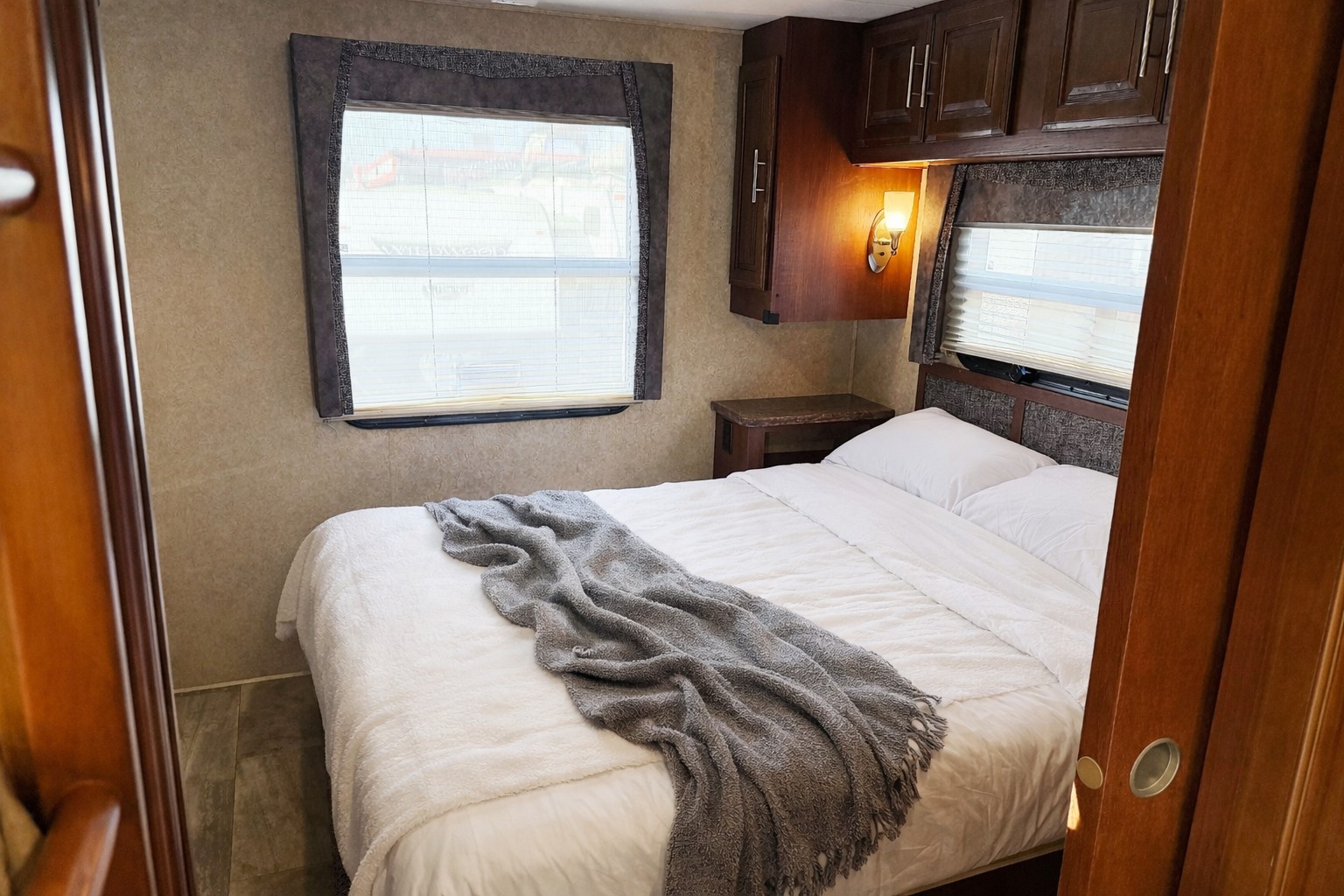 Relaxing RV rental bedroom: comfortable bed with gray throw, window with blinds, and dark wood overhead cabinets.. Forest River Georgetown 2016