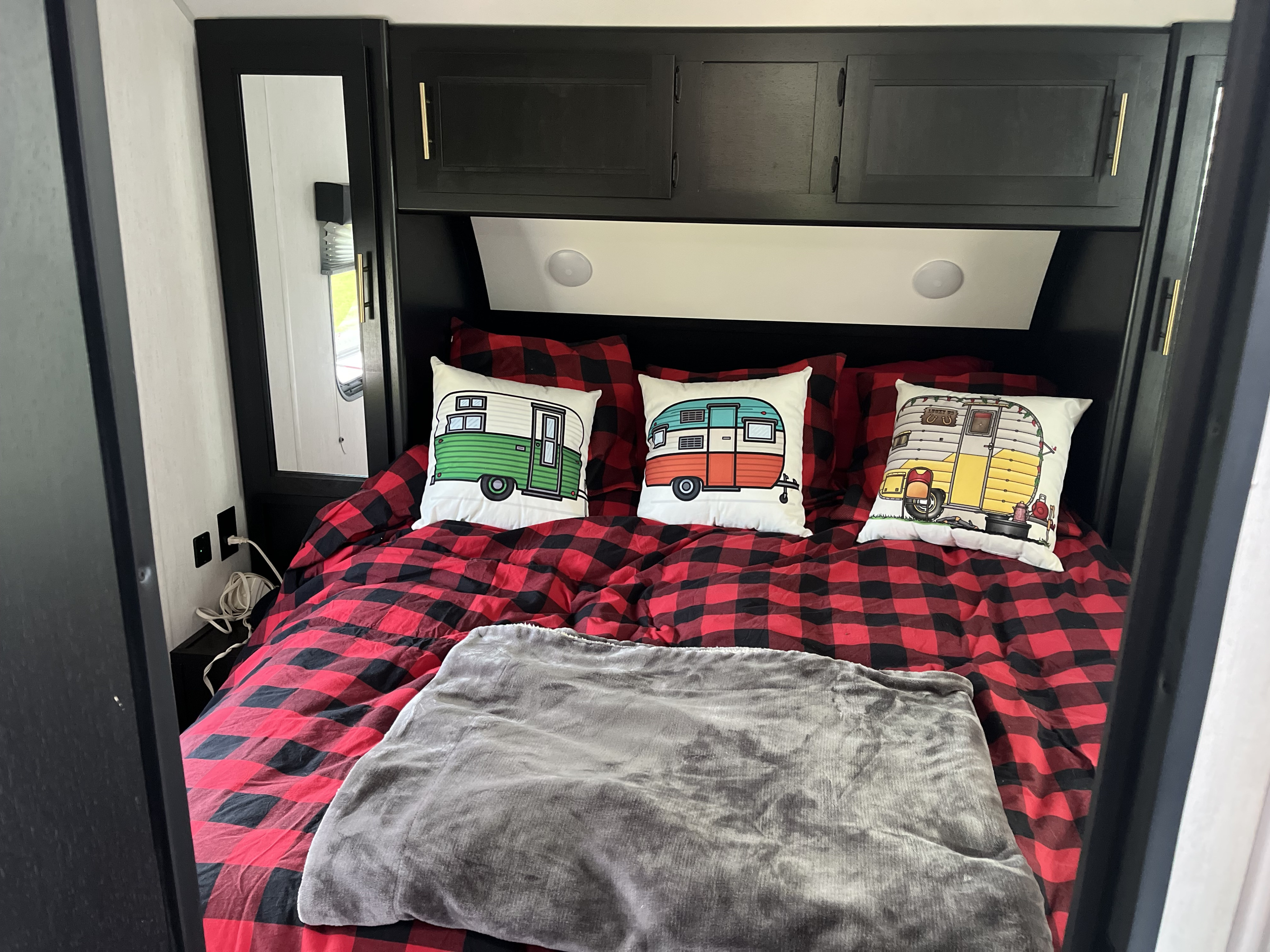 Cozy RV rental bedroom with buffalo plaid bedding, vintage camper pillows, and overhead cabinets. Relax in comfort!. Forest River Cherokee 2022
