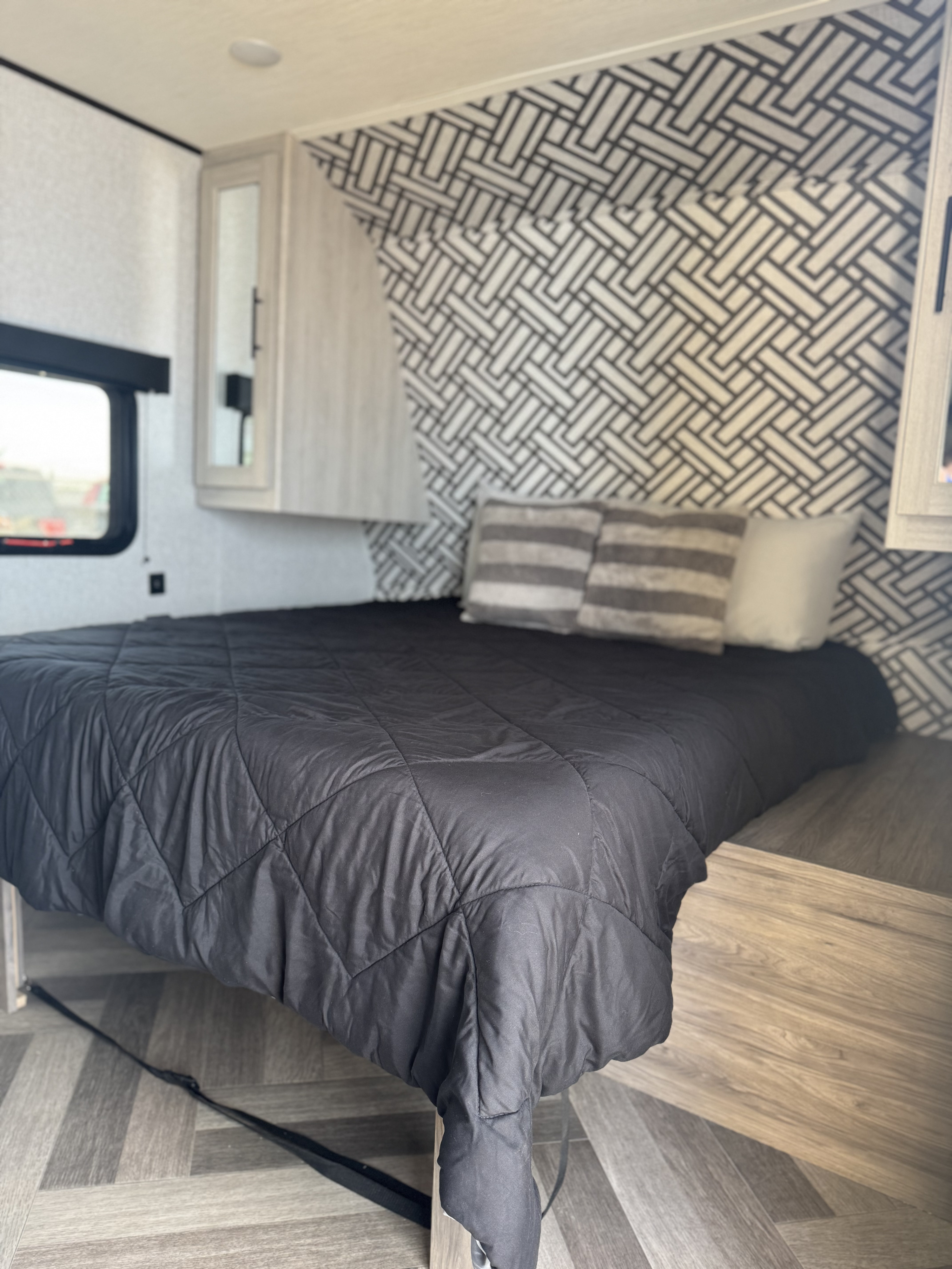 RV rental bedroom: Bed with black comforter, patterned wall, and wood-look floor. Modern and comfortable interior.. Crossroads RV Zinger Lite 2024