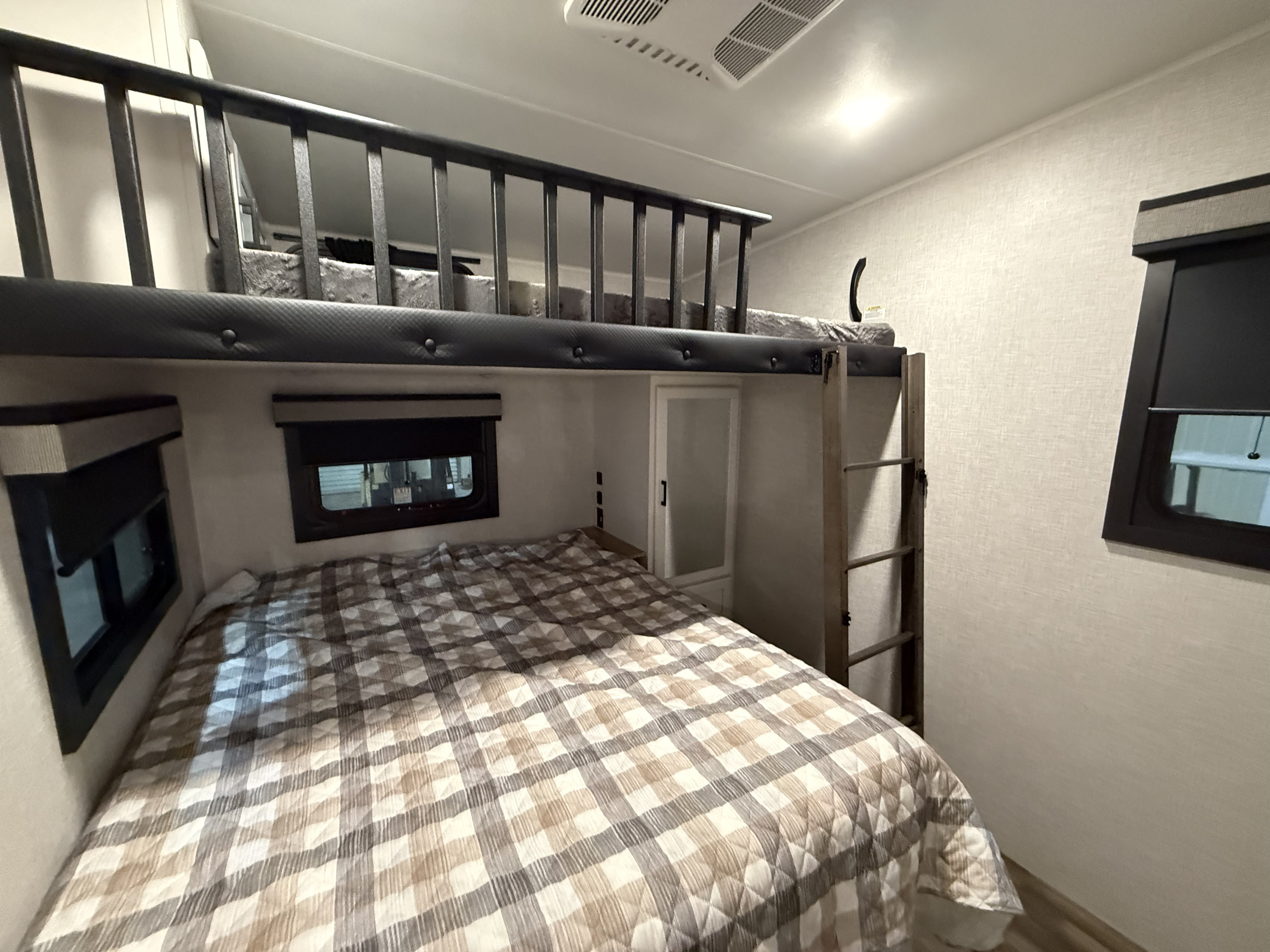 RV rental bedroom with a plaid lower bed, upper bunk bed with safety railing, ladder, and windows. Cozy mobile sleeping area.. Jayco Eagle 2025