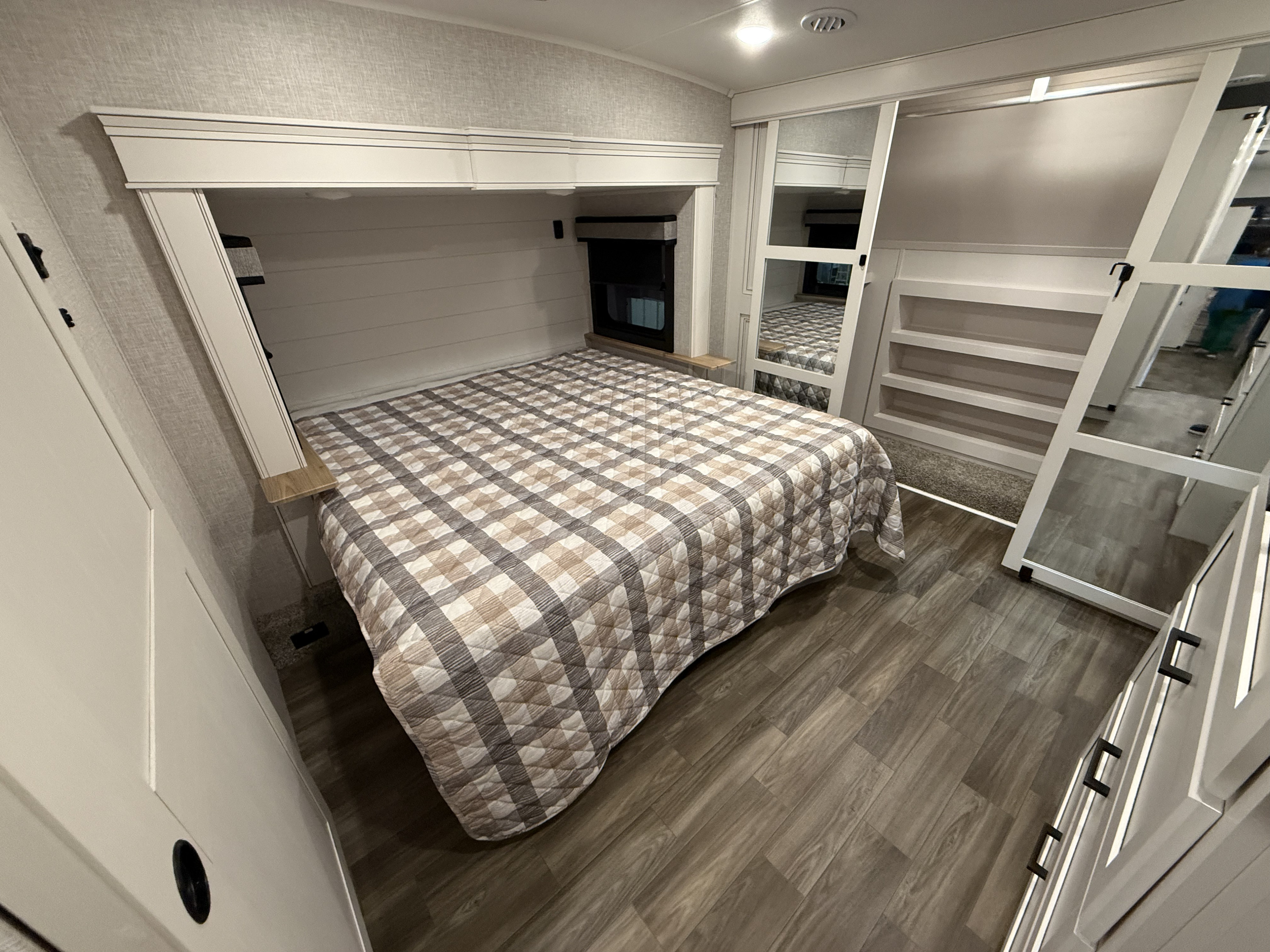 Cozy RV rental bedroom with a plaid bed, built-in storage, wood-look flooring, and mirror details for compact living.. Jayco Eagle 2025