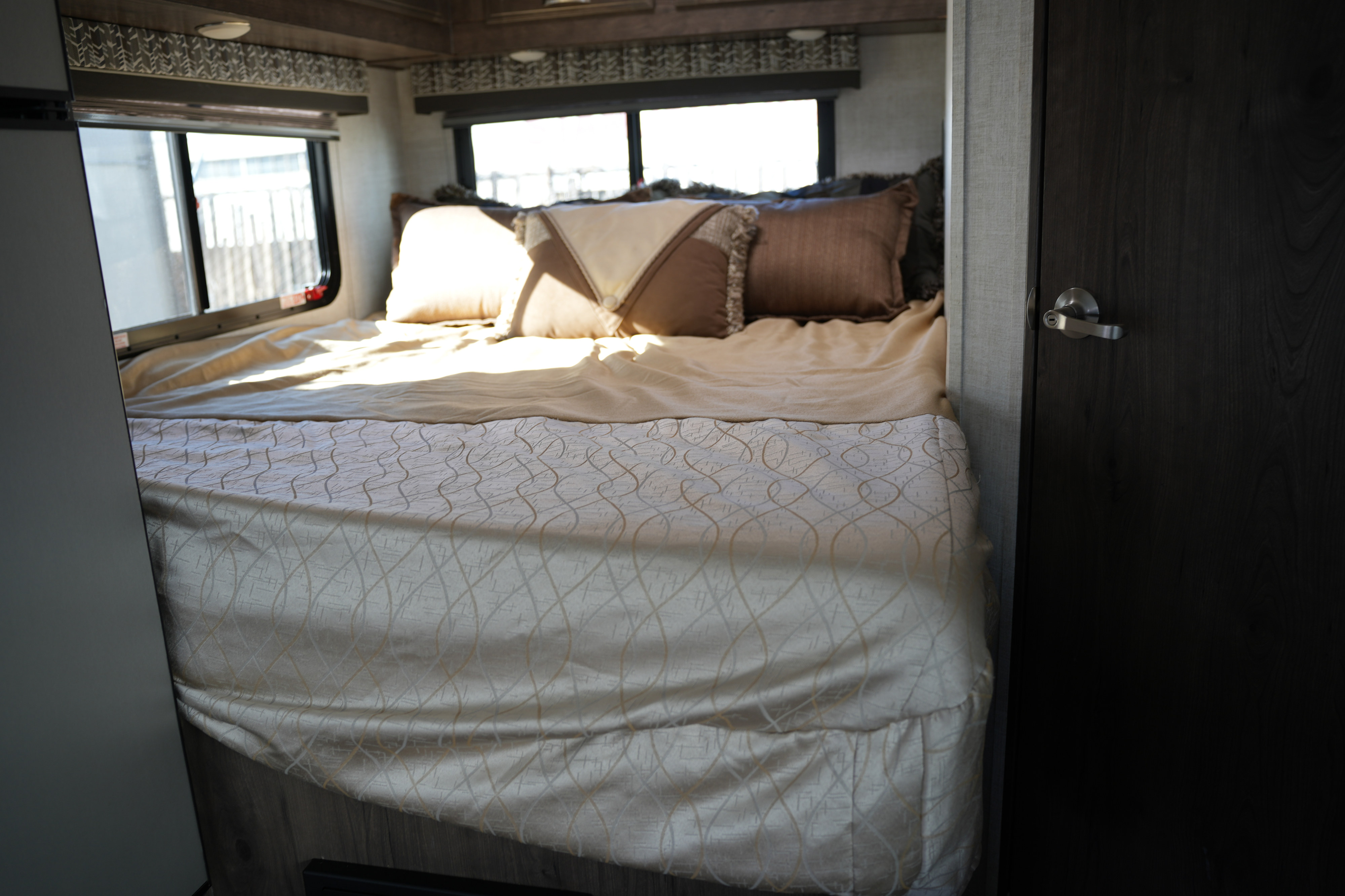 Cozy rv rental bedroom featuring light-colored bedding, decorative pillows, and windows allowing natural light.. Gulf Stream Conquest 2023