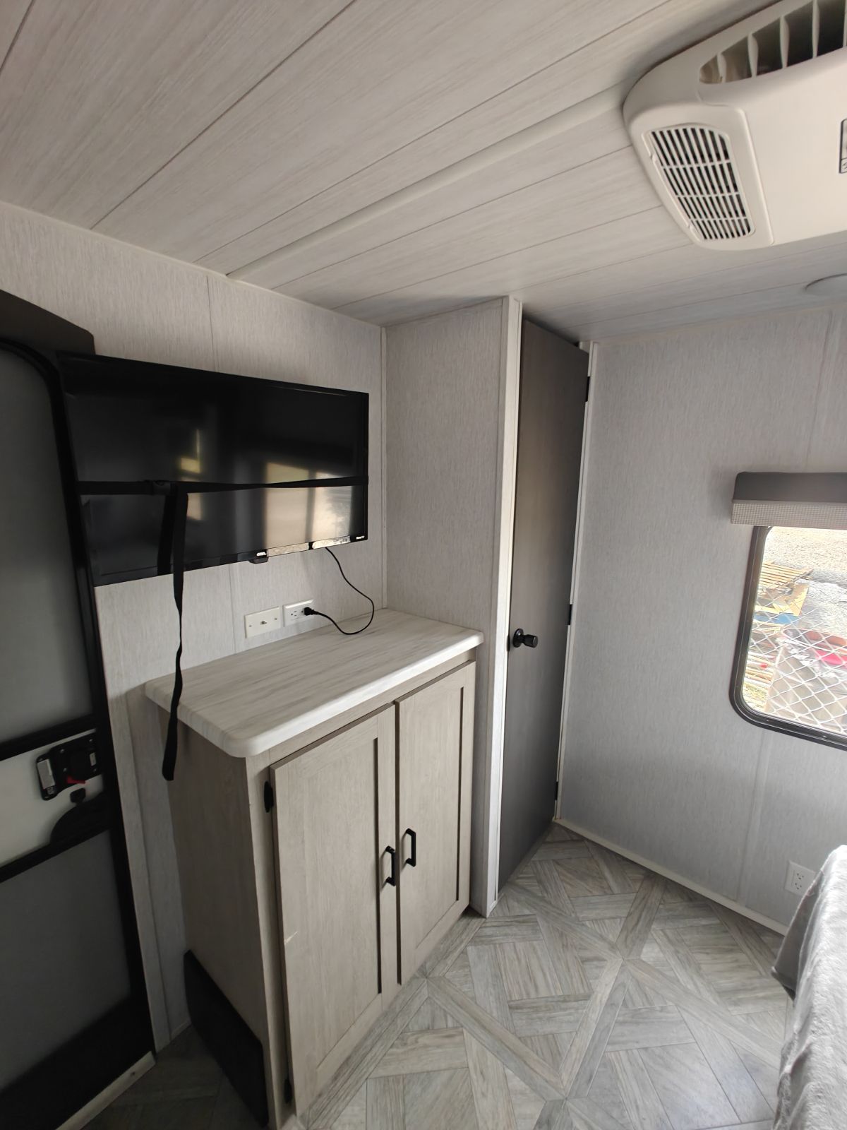 Modern RV rental interior showing a light-colored bedroom with wall-mounted TV, storage, and AC unit.. Forest River Salem 2024