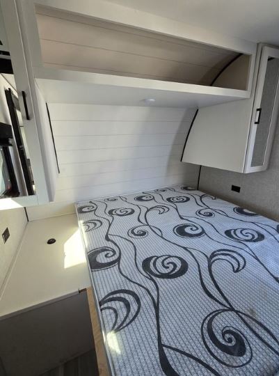 RV rental bedroom: Modern white interior with a patterned mattress, shiplap-style walls, and overhead storage.. Starcraft Autumn Ridge 2022