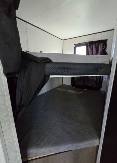 RV rental bunk beds with dark gray mattresses, side safety net, and window with curtain, offering compact sleeping space.. Starcraft Autumn Ridge 2022