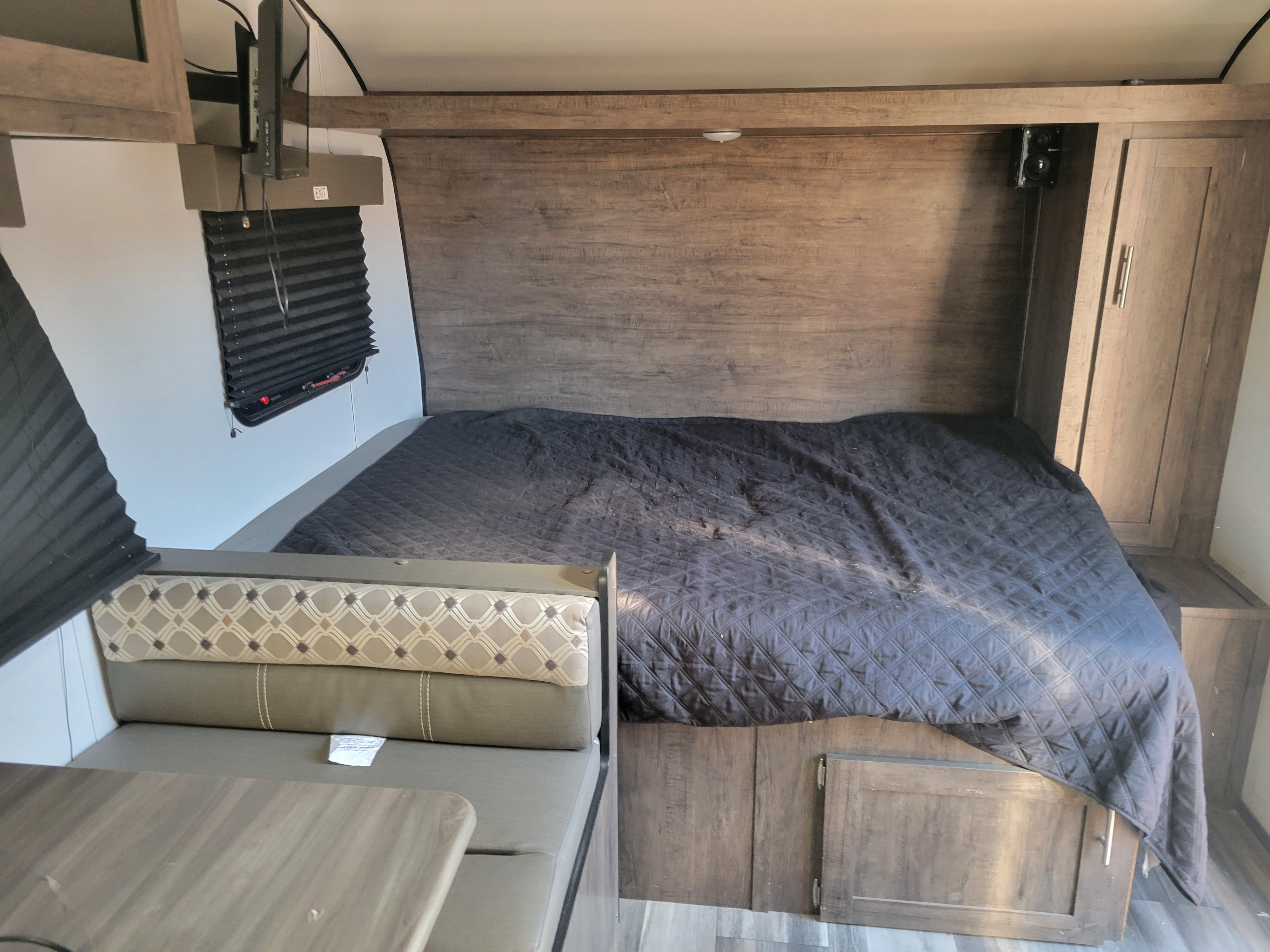 RV rental interior: a cozy bed with dark quilt, dinette, and media setup in a compact, wood-paneled space.. Riverside RV Retro 2022