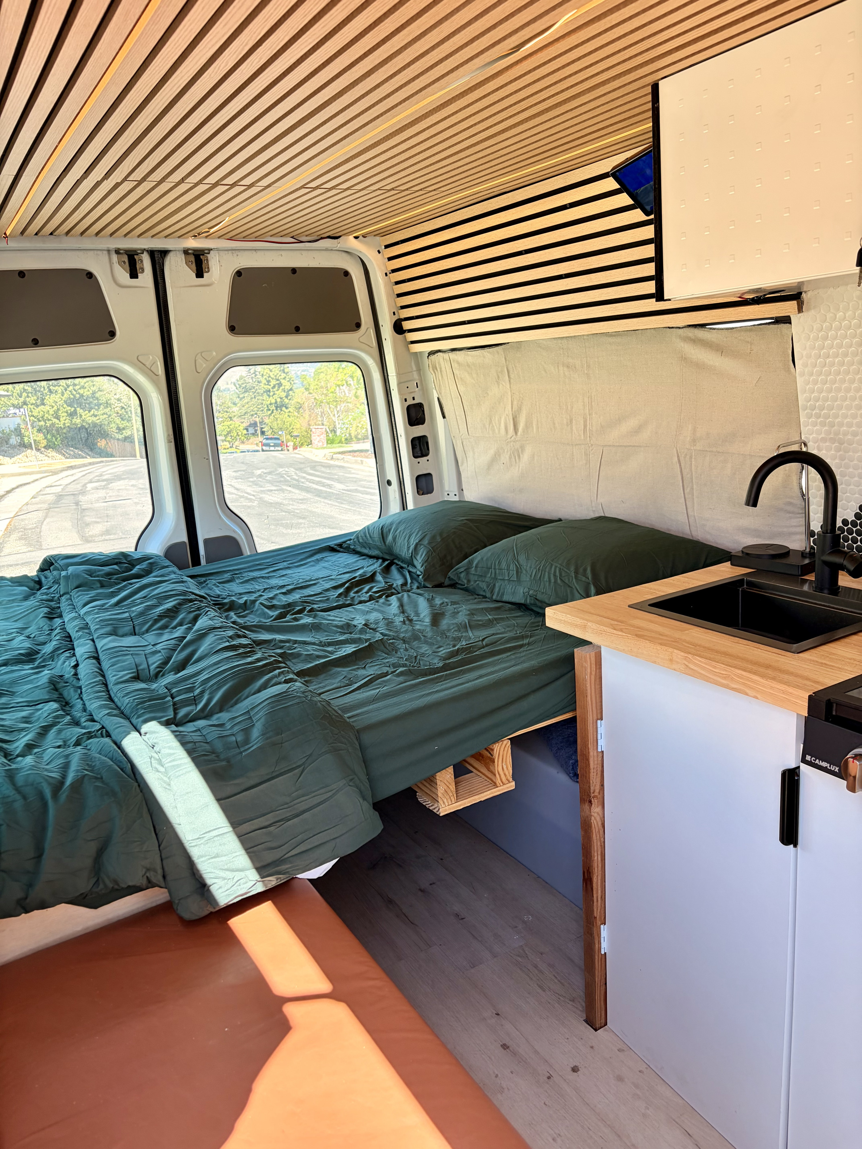 RV rental: Modern camper van interior with a bed featuring green sheets, a compact kitchenette, and wood slat paneling.. Mercedes-Benz Sprinter 2008