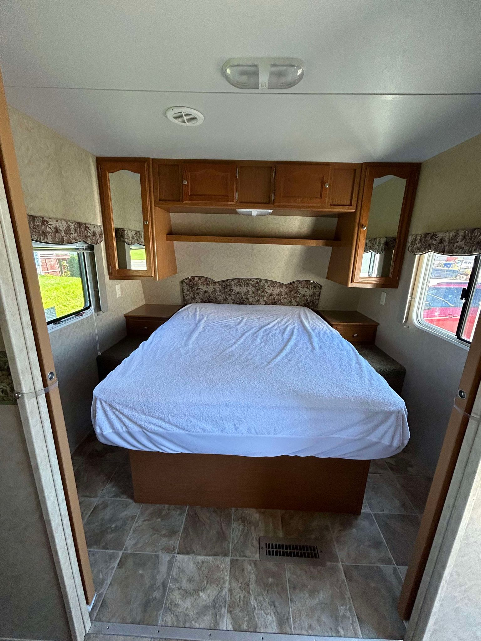 Spacious RV rental bedroom with a bed covered in white, wood cabinetry, side windows, and a tiled floor. Bright interior lighting.. Dutchmen Dutchmen 2007