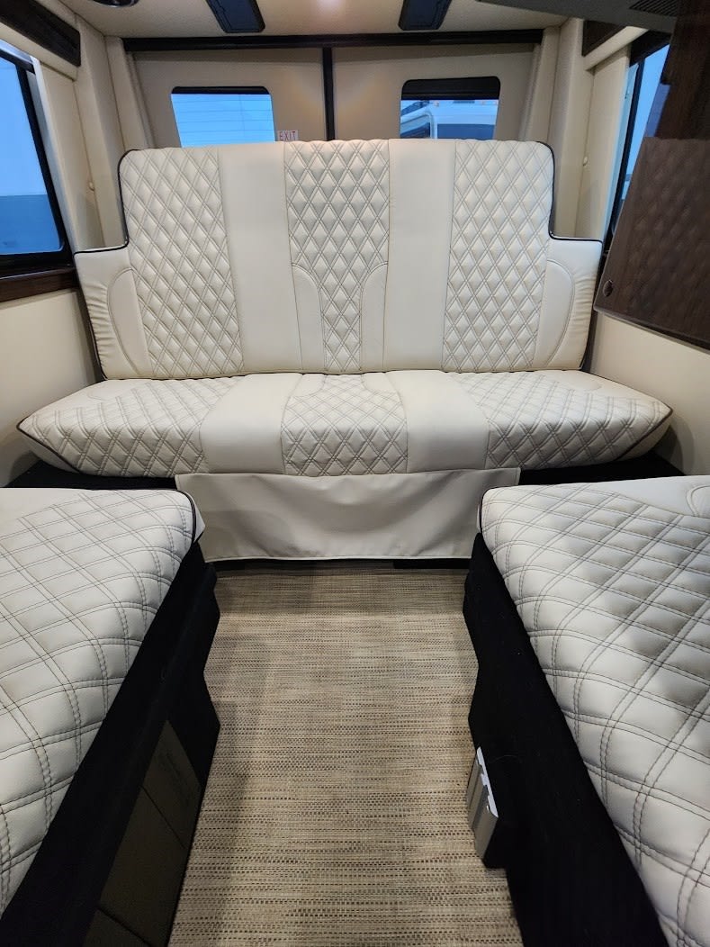 Luxurious white quilted interior of an RV rental, featuring a large bench seat and two side beds. Perfect for comfortable travel.. Midwest Automotive Designs Patriot 2023