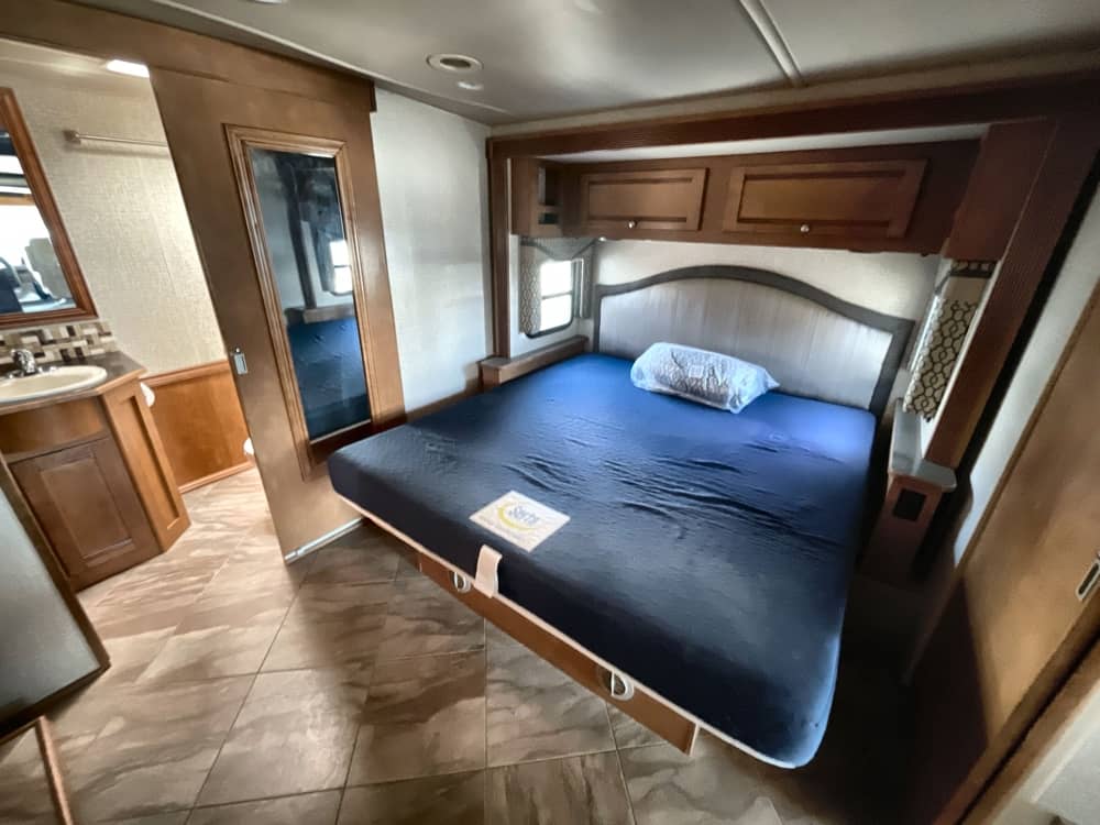 Spacious RV rental bedroom: blue bed, vanity, and mirrored sliding door. Your comfy home on wheels awaits.. Winnebago Sunova 2019