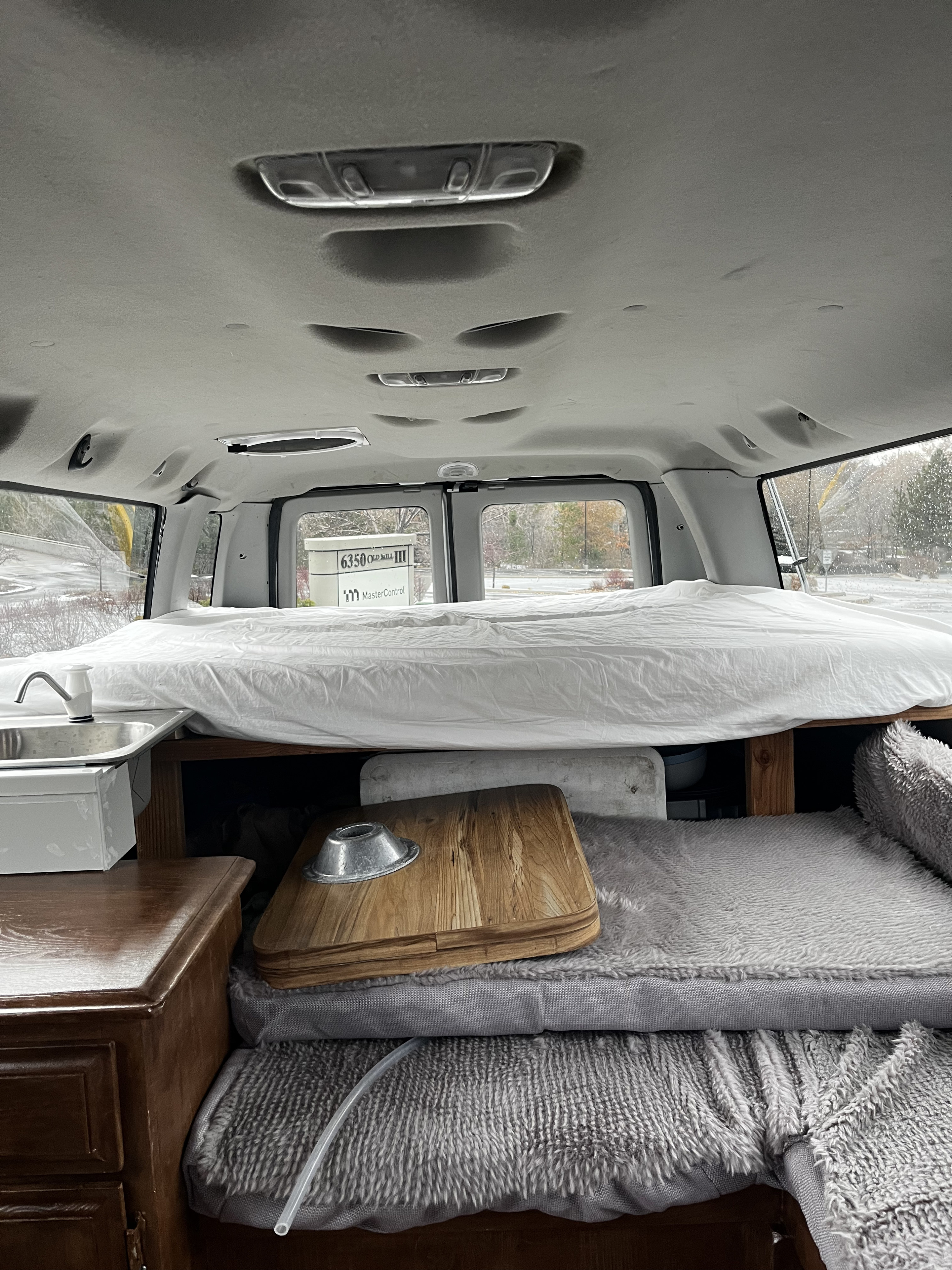 Cozy RV rental interior: bed, sink, and storage in a custom camper van conversion. Perfect for mobile living.. Ford E350 Box Van 2015