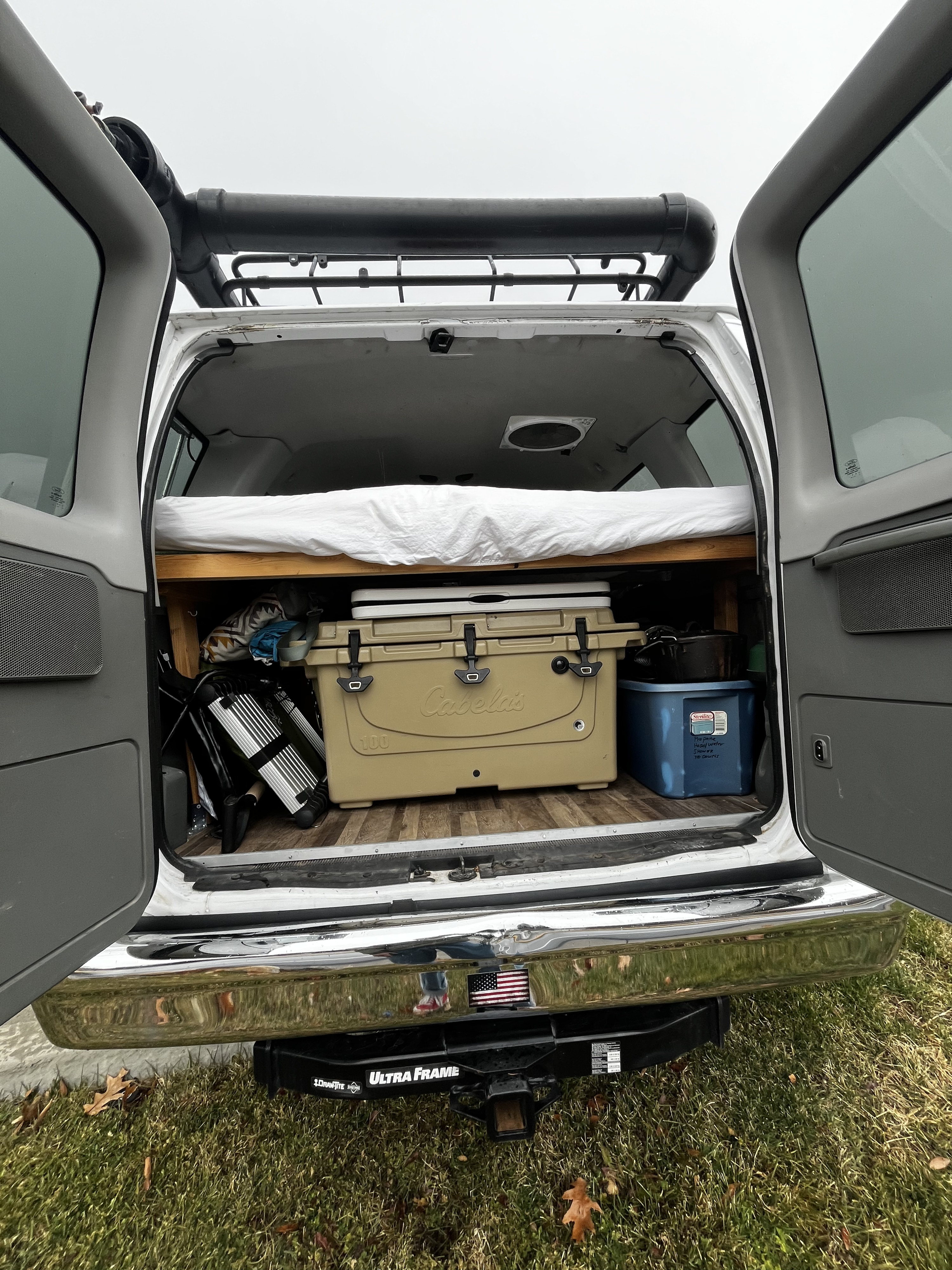 RV rental van's organized back: bed, cooler, camping gear, roof rack, & hitch visible. Ready for adventure.. Ford E350 Box Van 2015