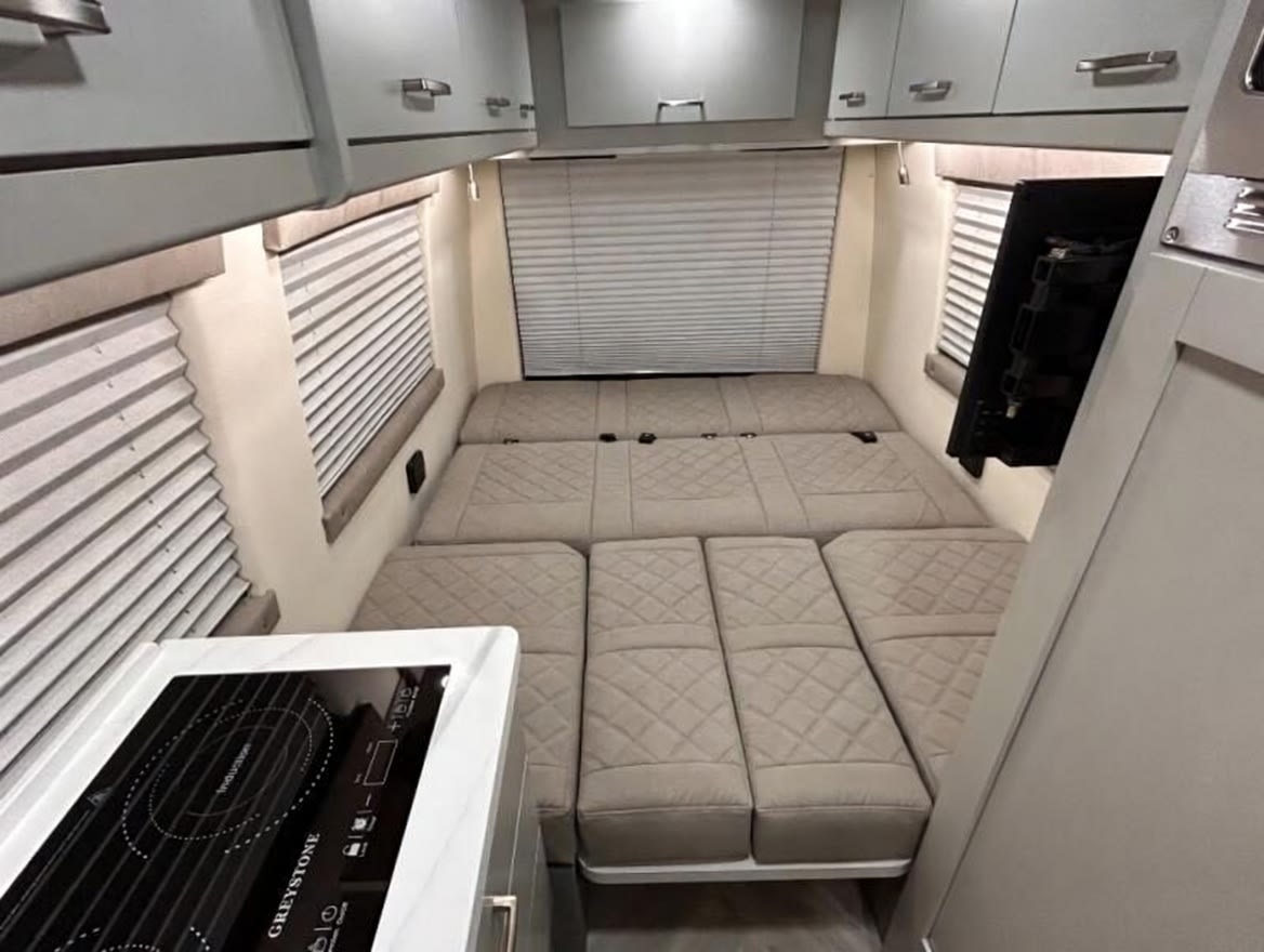Compact rv rental interior with a cozy, segmented bed, induction cooktop, and ample overhead storage.. Forest River Coachmen Galleria 2025