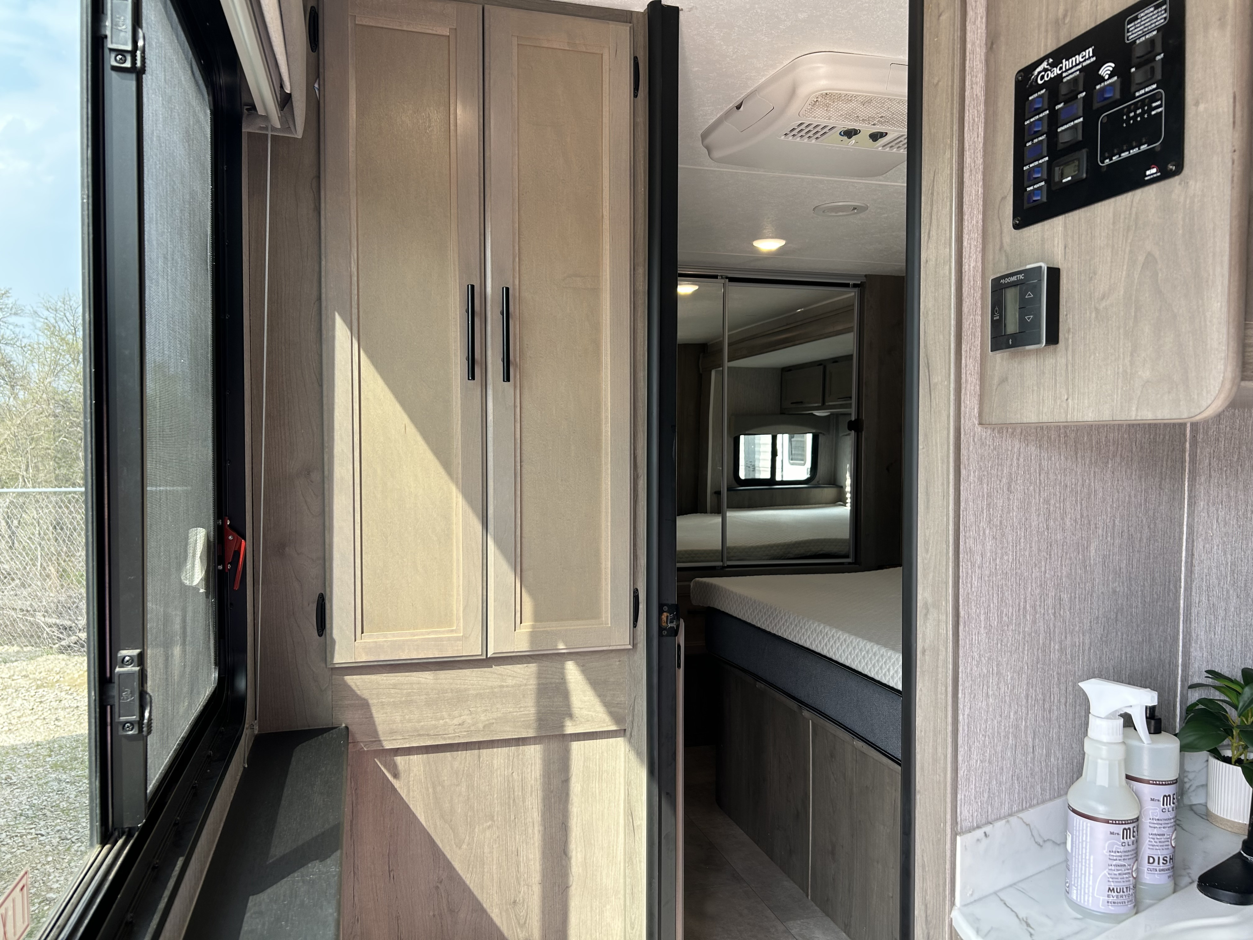 RV rental interior features modern cabinets, a bright window, Coachmen/Dometic controls, and a peek into the cozy bedroom.. Coachmen Freelander 2021