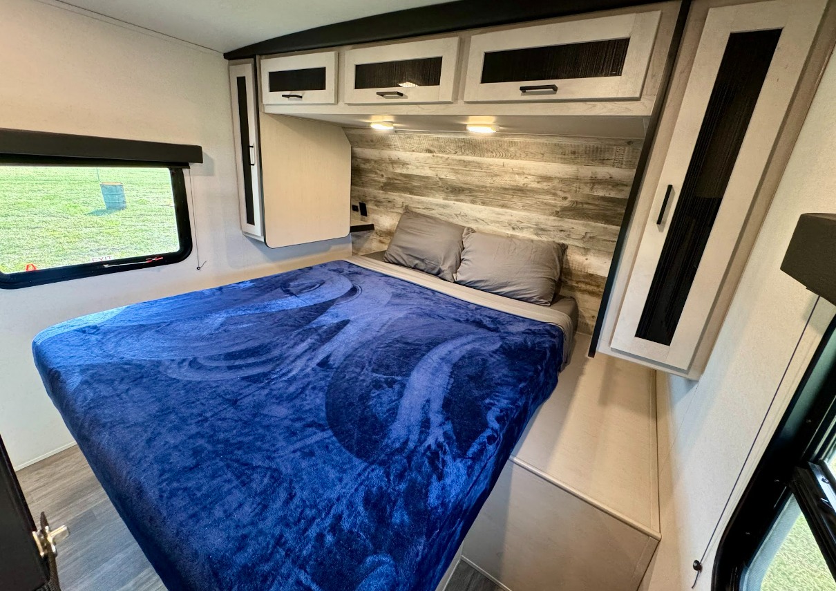 Modern RV rental bedroom featuring a comfortable bed, stylish accent wall, overhead cabinets, and a window.. Mallard M32 2024