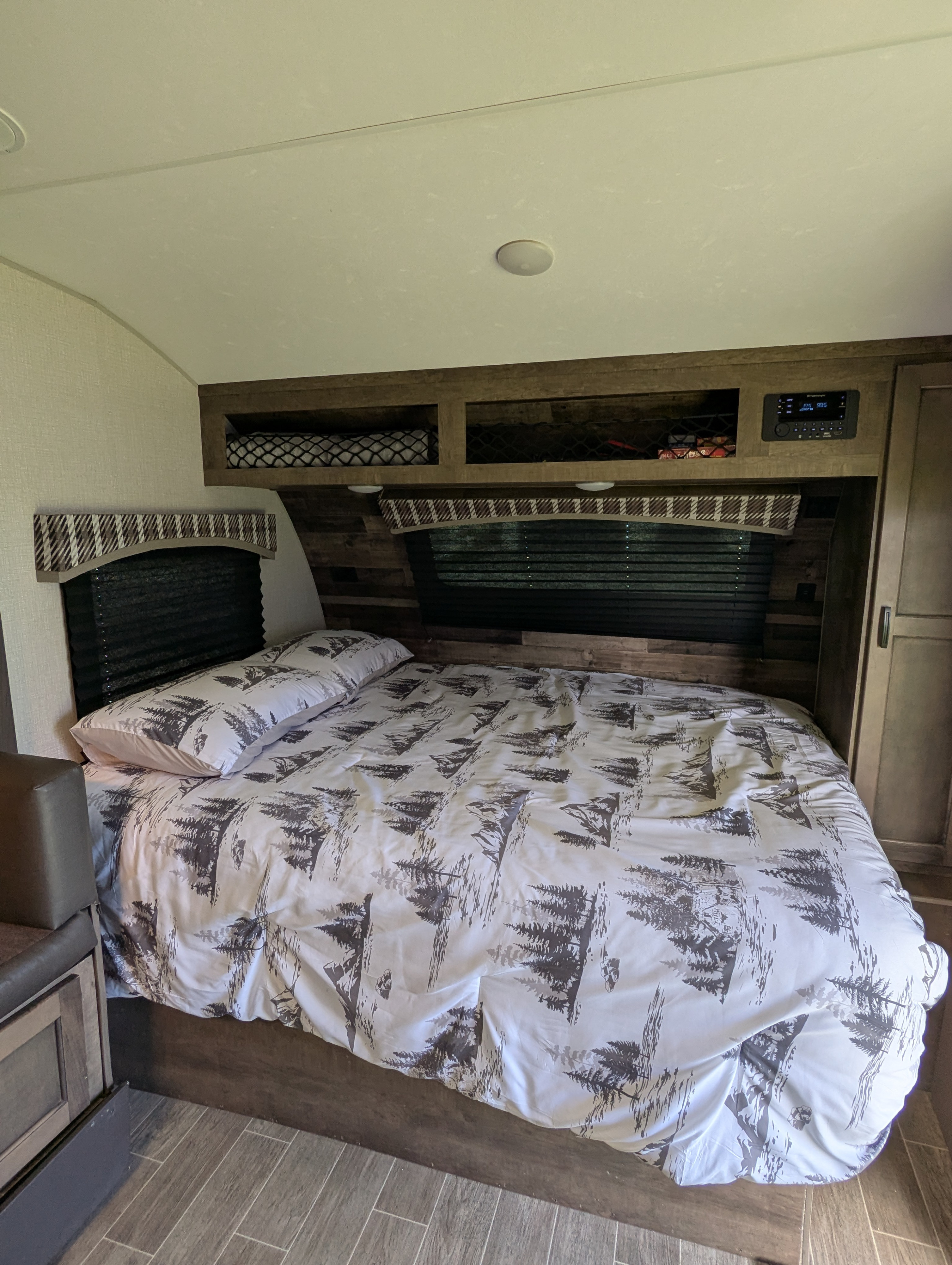 RV rental bedroom features a cozy bed with nature-themed bedding, overhead storage, and an entertainment system.. Sonic Lite 2021