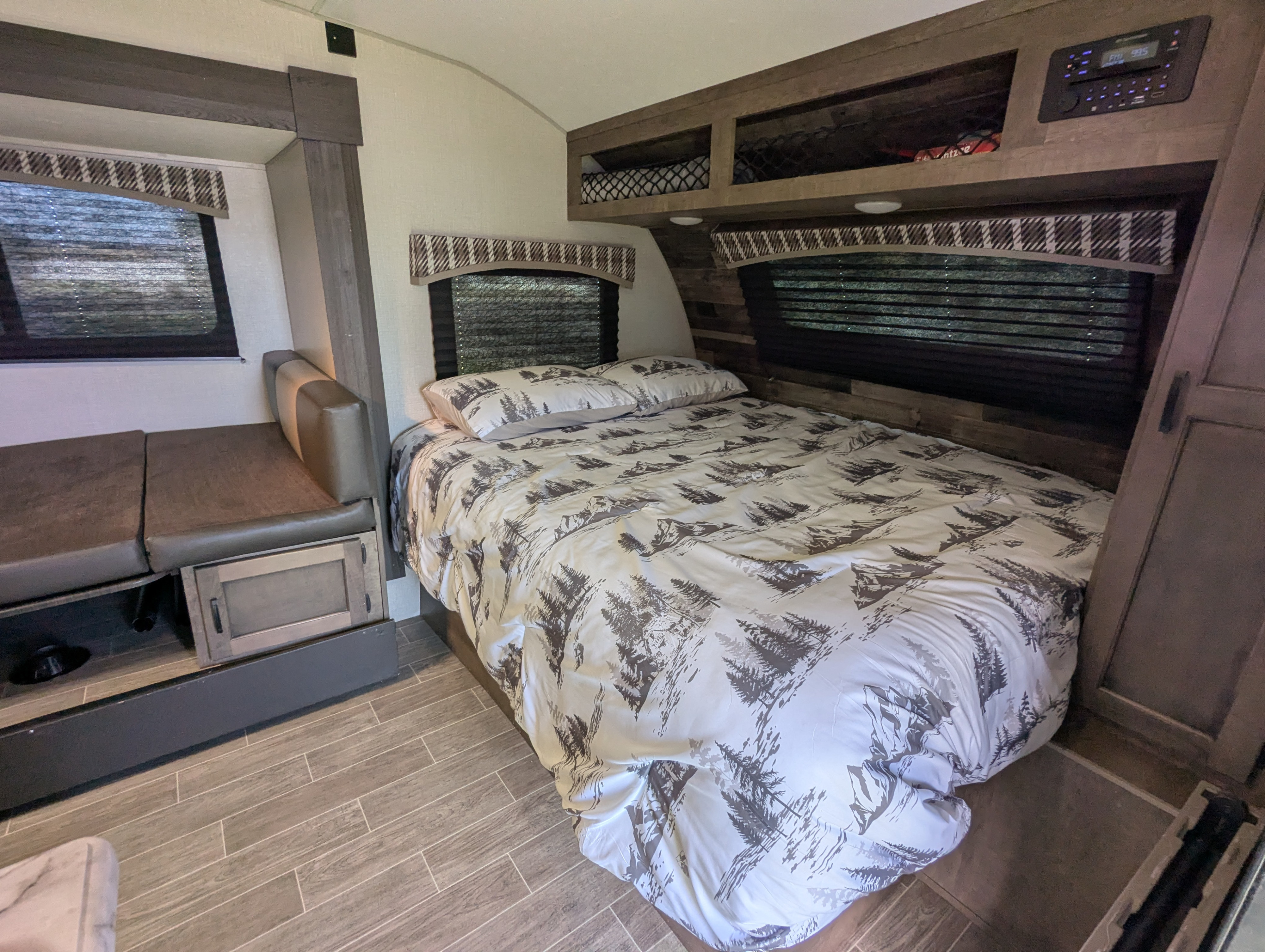Cozy rv rental bedroom interior featuring a bed with nature-themed bedding, a compact dinette, and overhead storage.. Sonic Lite 2021