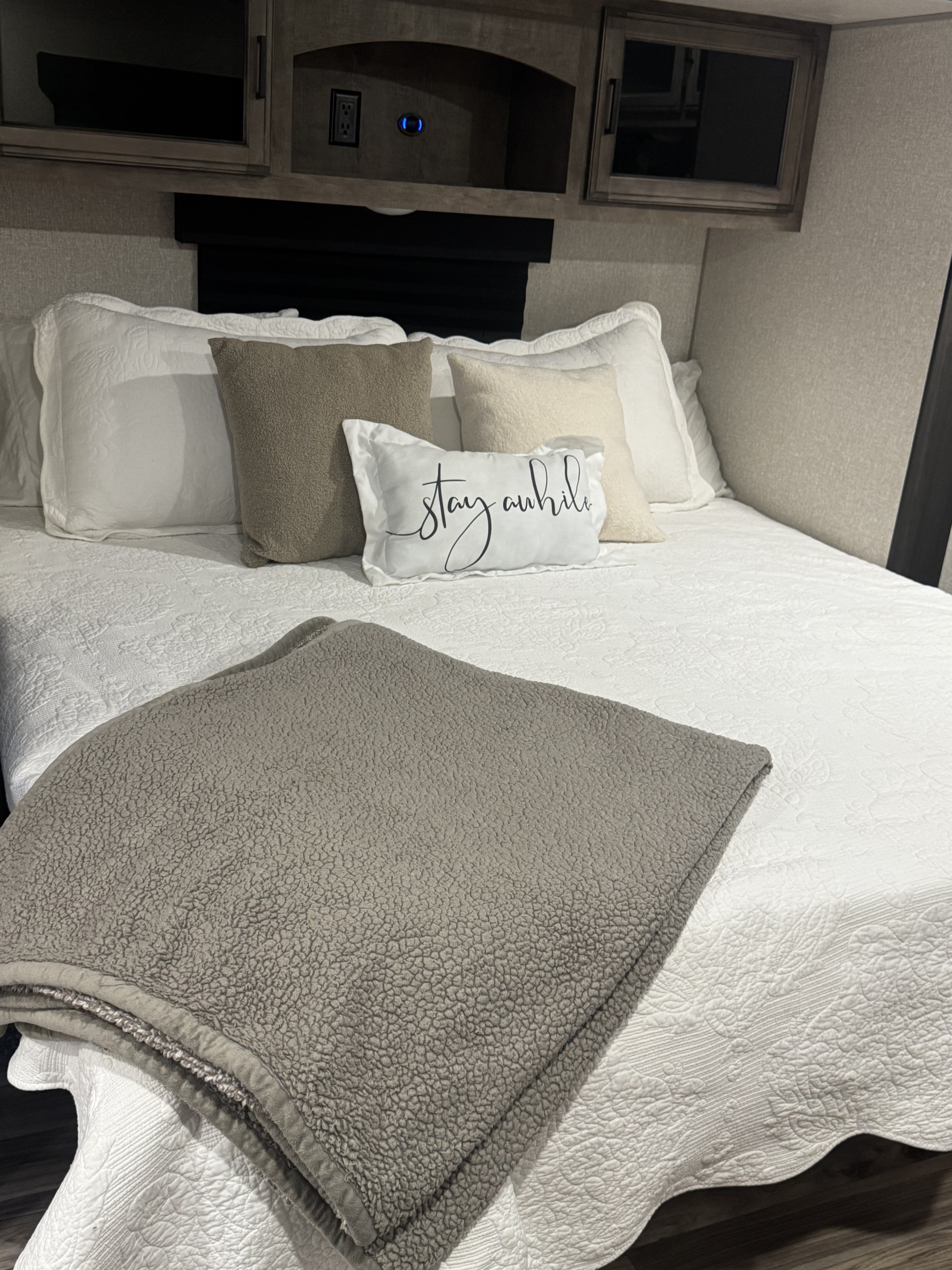 Cozy RV rental bedroom with white quilted bedding, neutral pillows, and a soft grey blanket. Overhead cabinets provide storage.. Sport Trek Touring Edition 2023