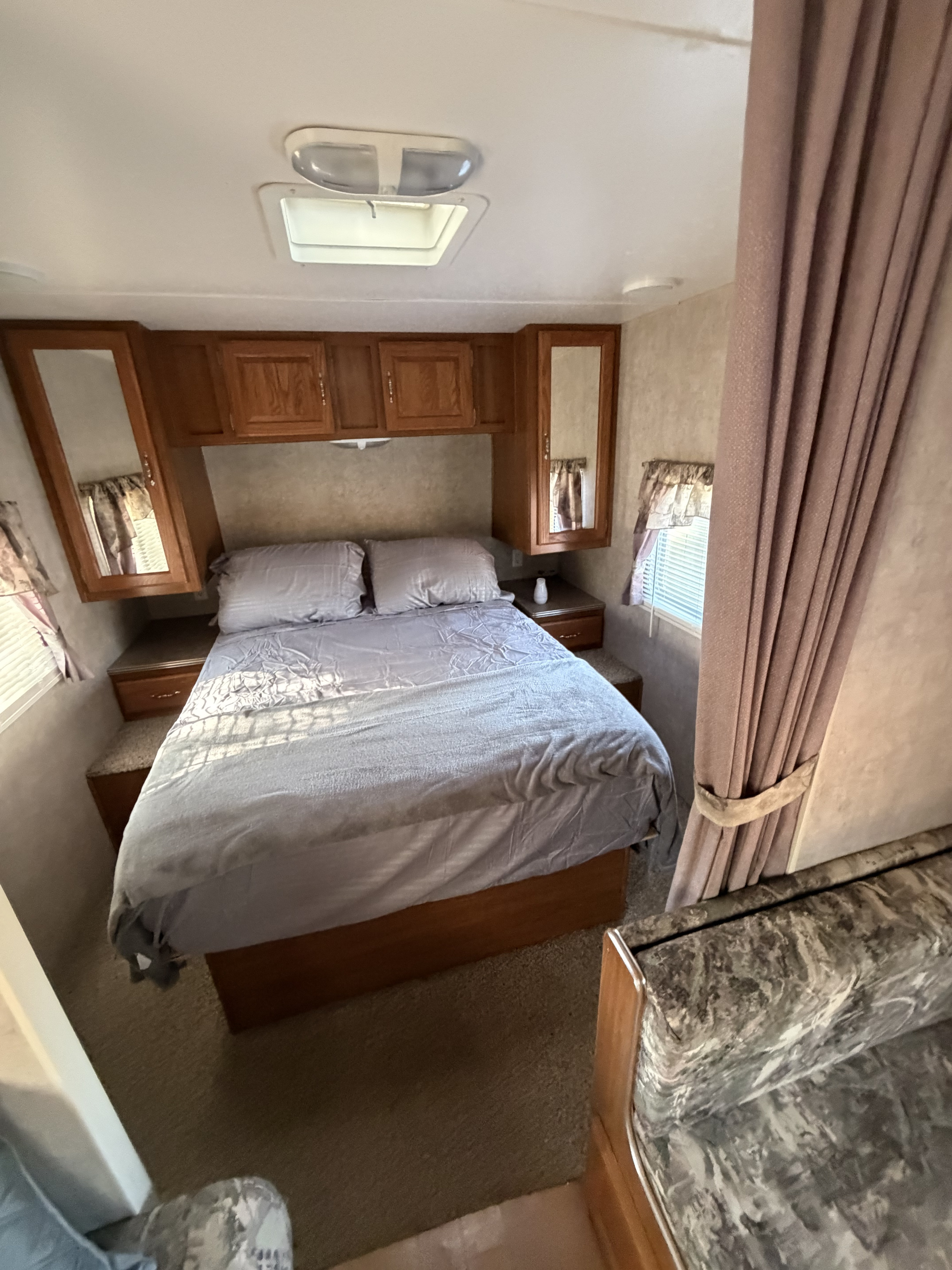 Compact RV rental bedroom with a gray bed, wooden overhead cabinets, mirrored storage, and windows.. Sun Valley Roadrunner XL 2005