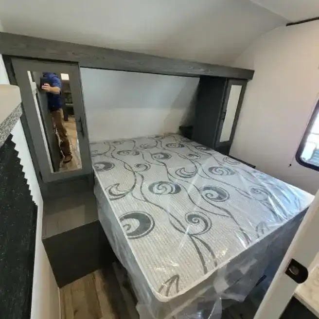 Discover this RV rental's cozy bedroom, featuring a new, plastic-covered mattress, mirrored storage, and overhead cabinets.. Dutchmen Aspen Trail 2021