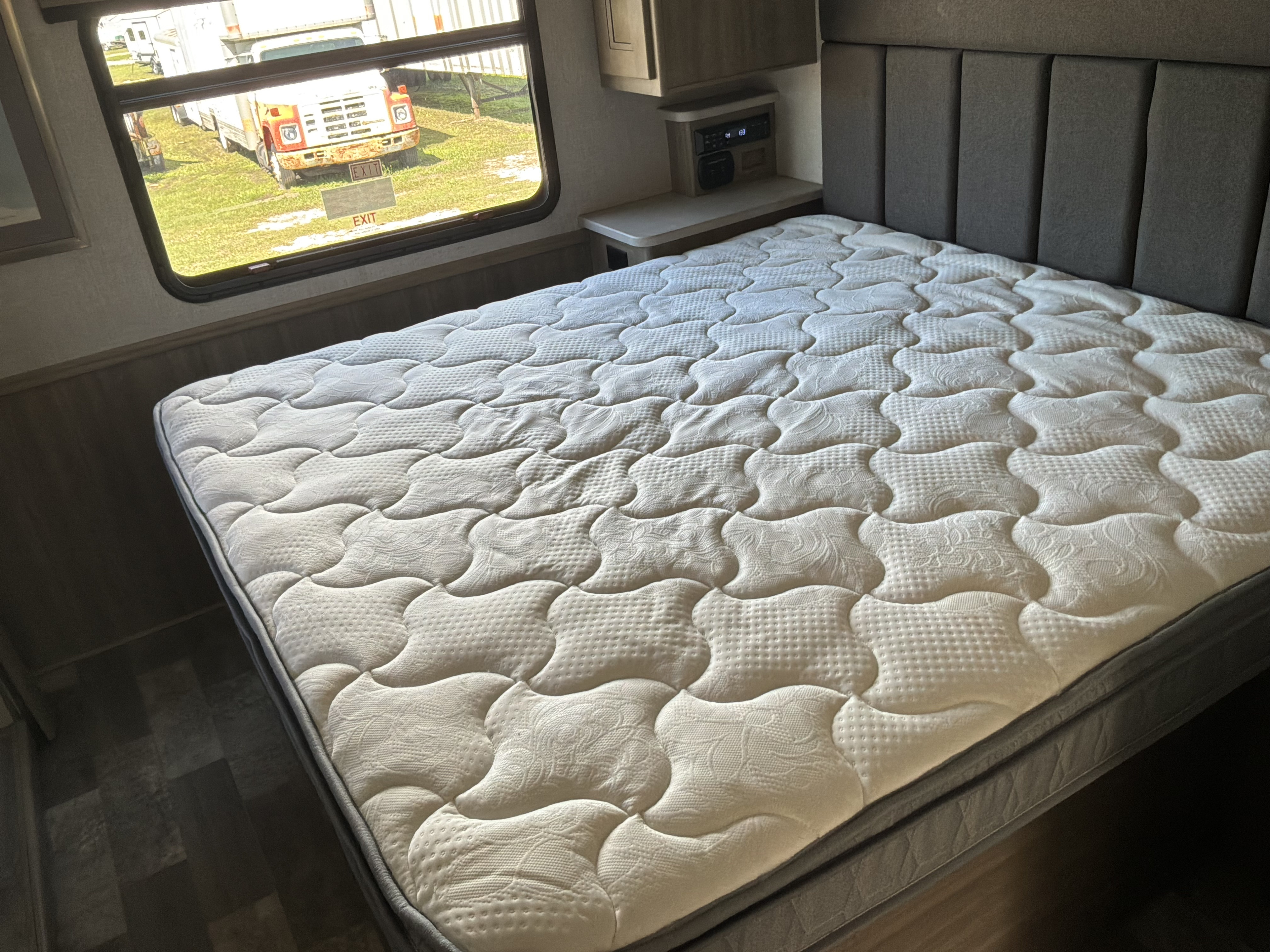 RV rental bedroom: a comfortable quilted mattress, built-in nightstand with controls, and a window view of a truck outside.. Forest River Coachmen Mirada 2020