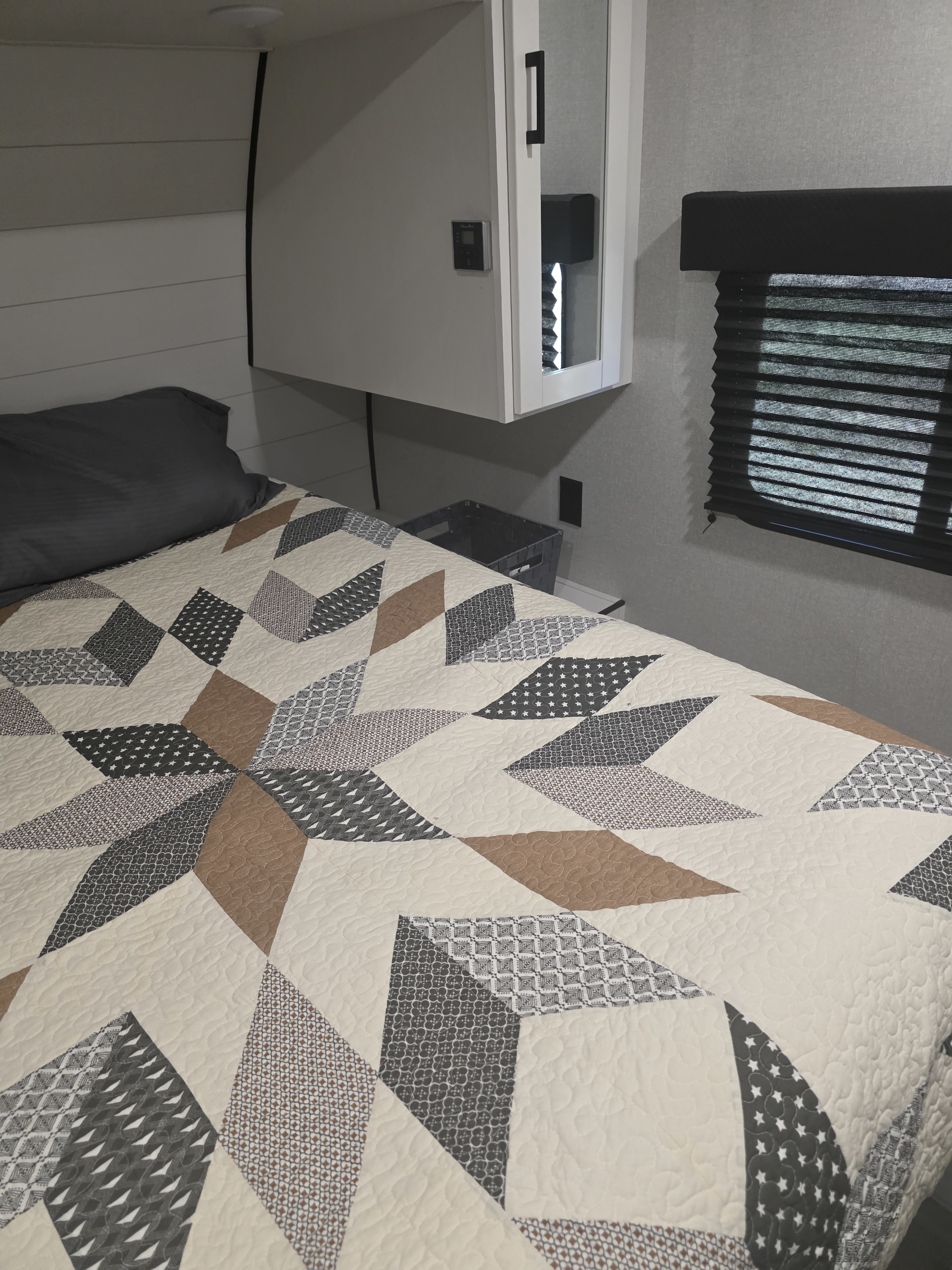 Cozy RV rental bedroom featuring a patterned quilt, dark pillow, white overhead cabinet, and a window with pleated blinds.. JAYCO JAY FLIGHT SLX 2026