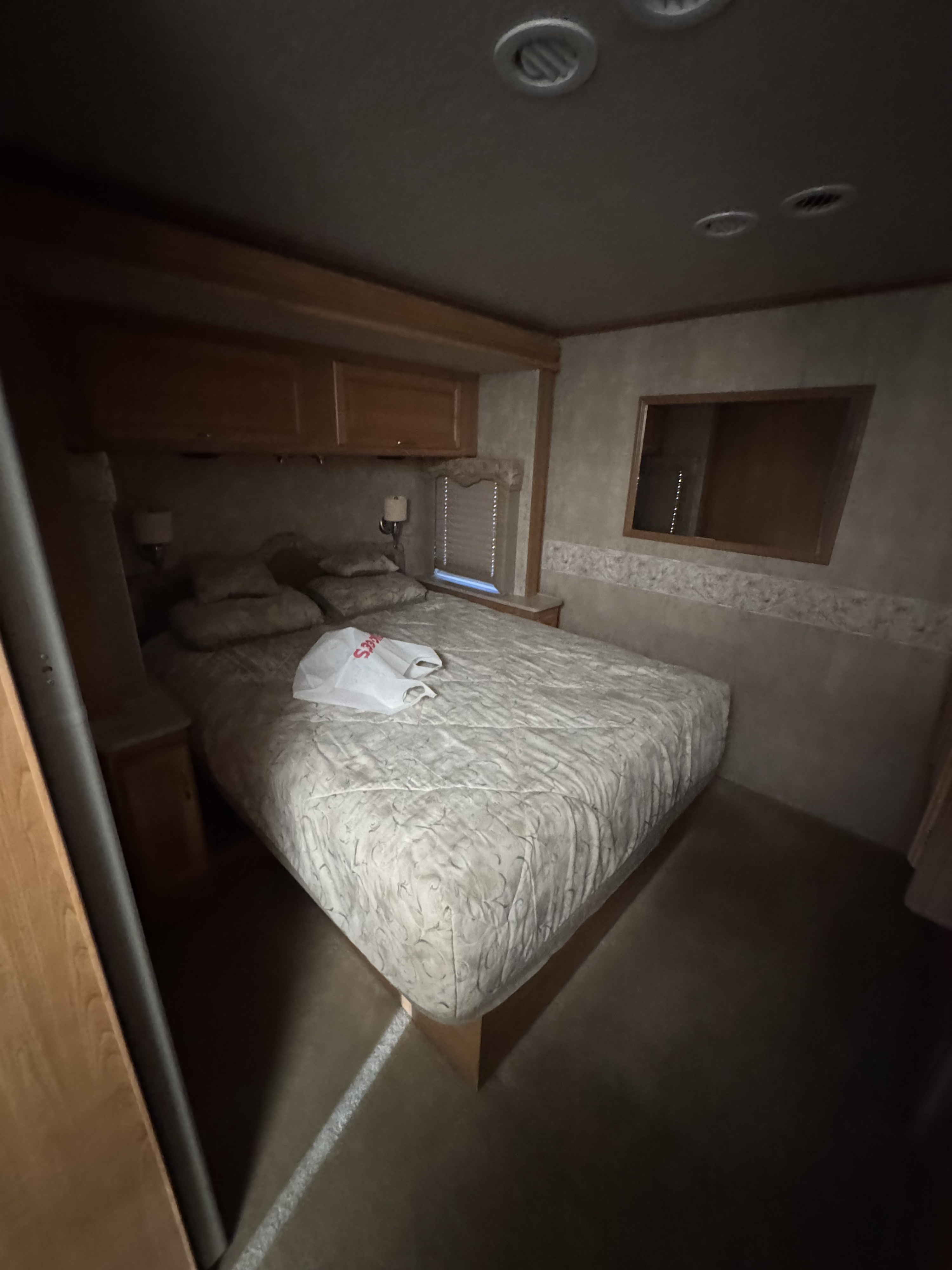 Cozy RV rental bedroom featuring a queen bed, overhead storage, window, and accent lighting.. Bounder Bounder Motorhome 2007