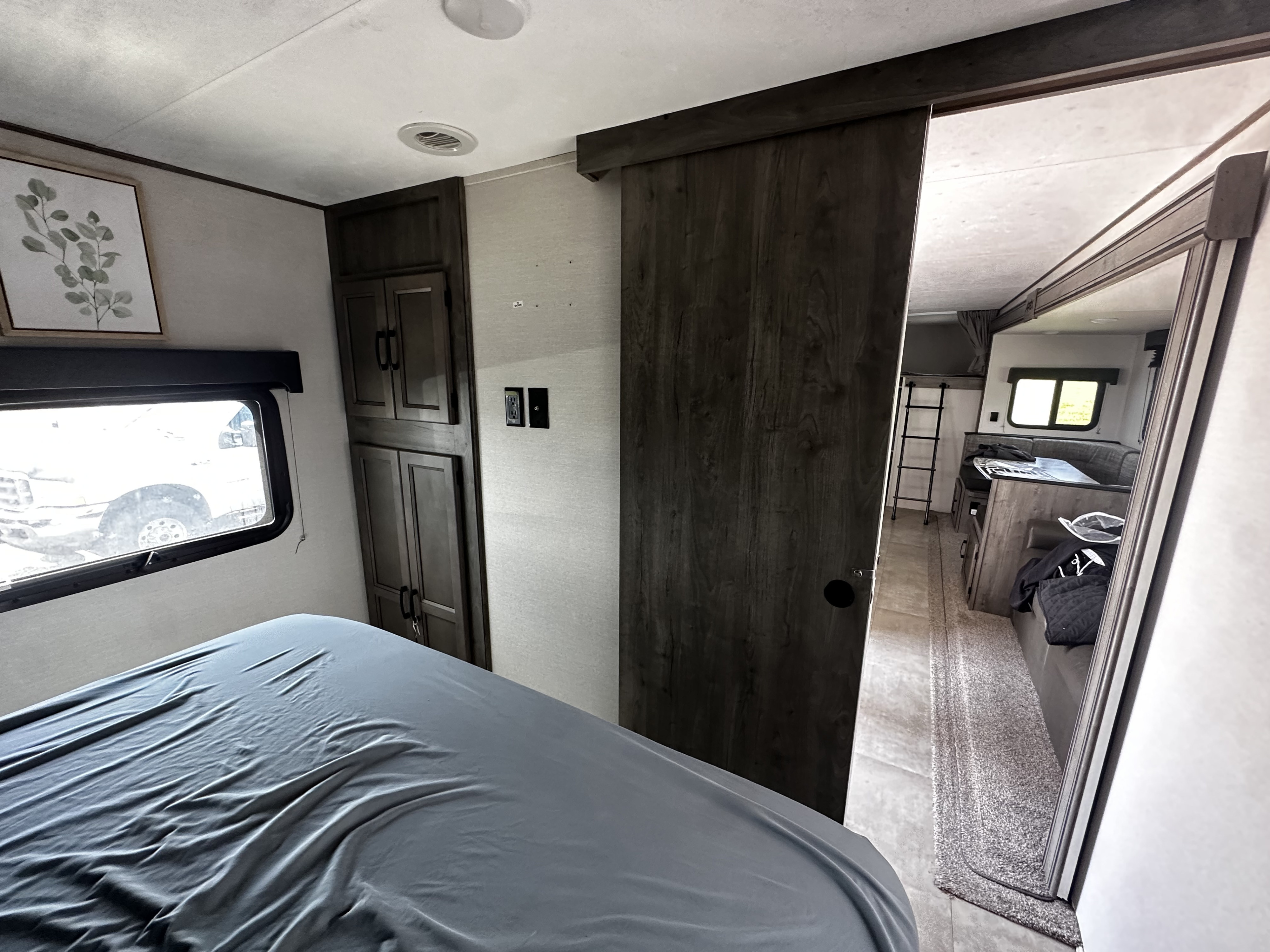 Cozy RV rental bedroom with bed, window, storage, and sliding door to living area with dinette and bunk ladder.. Coachmen Apex 2021