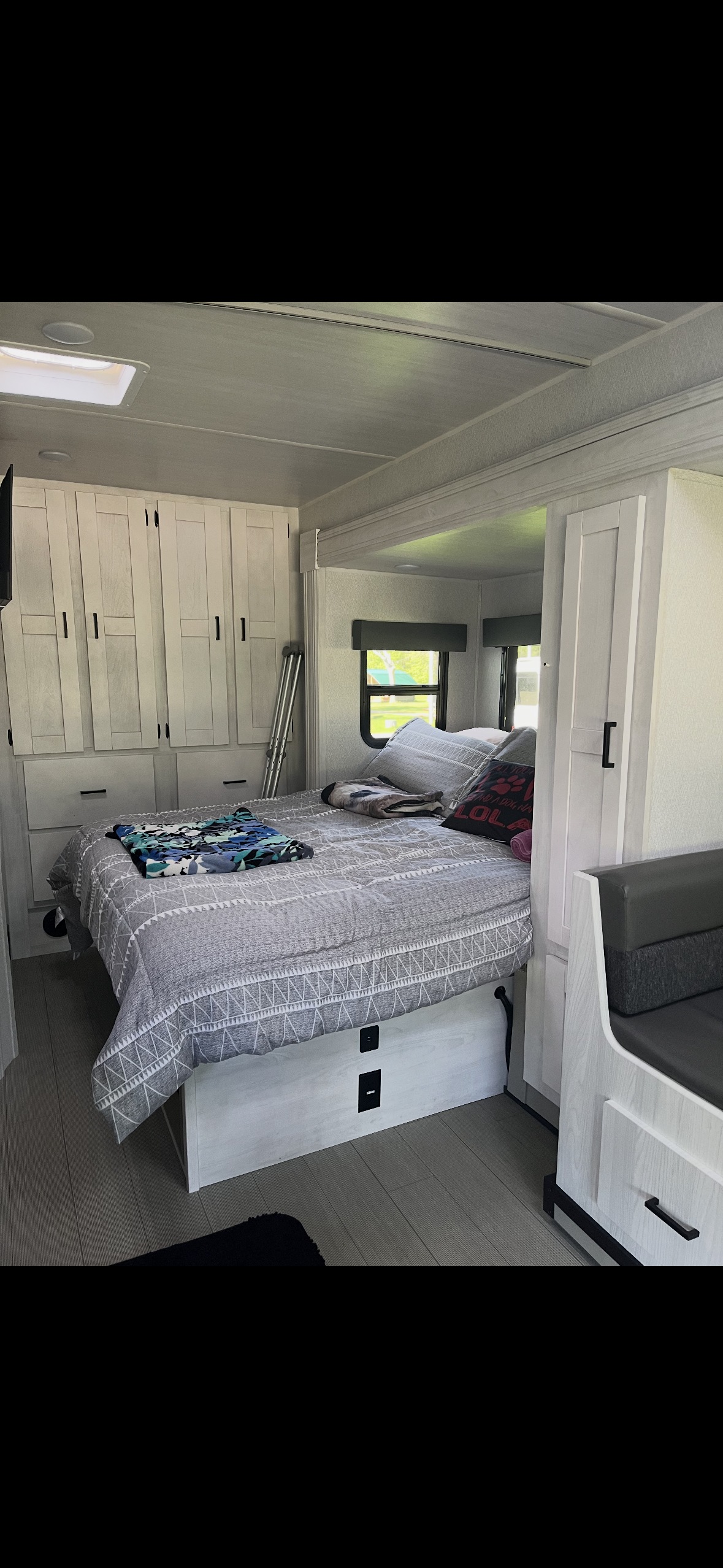 Bright RV rental bedroom: cozy bed, light wood storage, window view, and skylight. Perfect for travel adventures.. Forest River East to West Entrada 24FM 2023