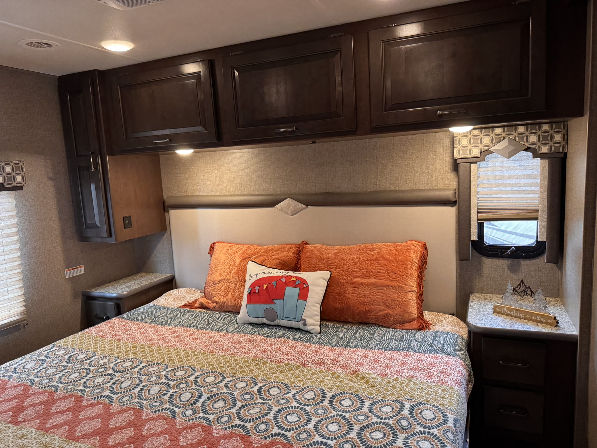 Experience this cozy rv rental bedroom, featuring a colorful quilt, camper pillow, and dark wood cabinets for storage.. Thor Hurricane 2020