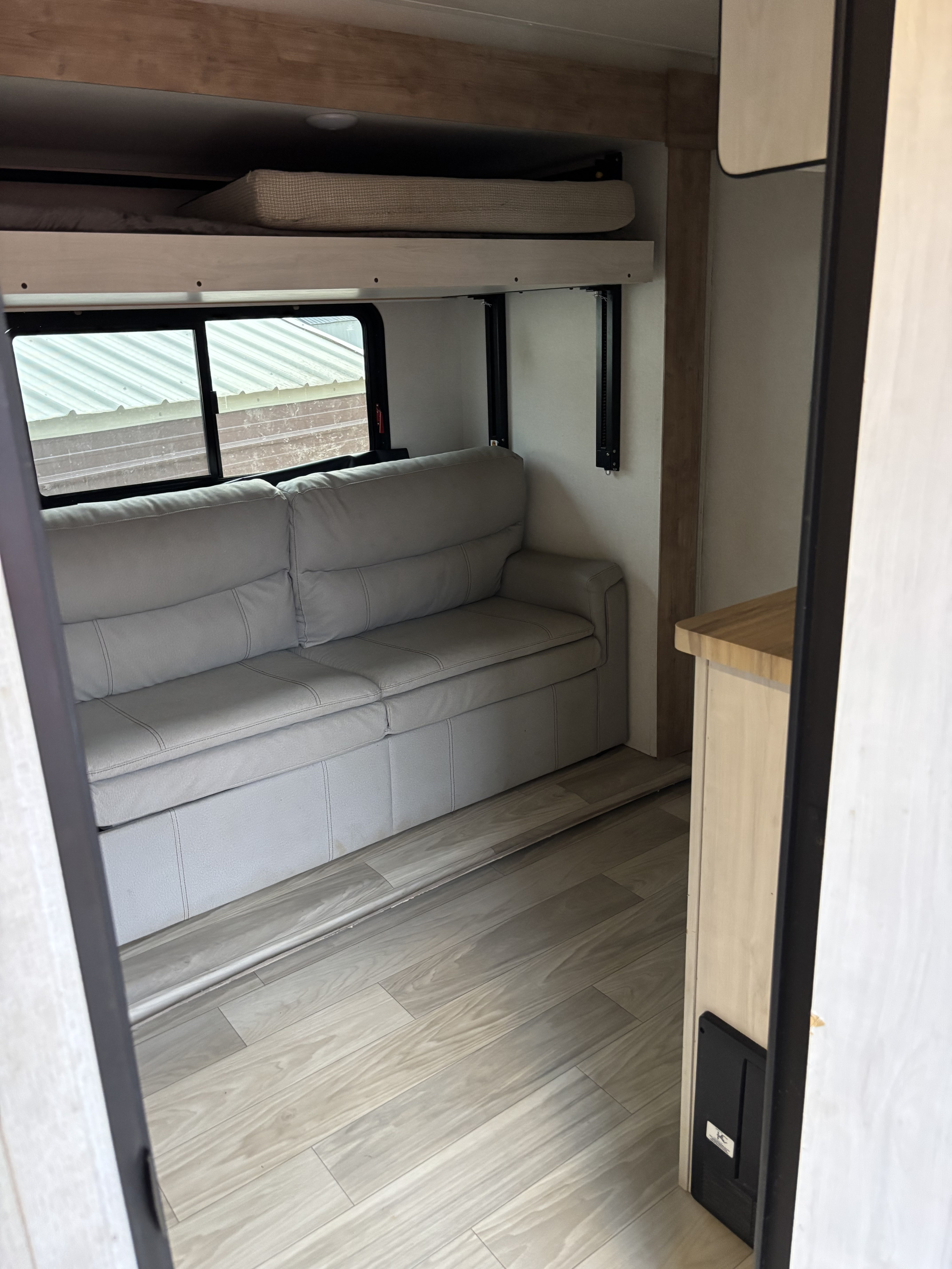 Step inside this RV rental's living area: a light gray sofa and bunk bed, with pale wood floors. A cozy, practical space.. Crusader Crusader Fifth Wheel 2023