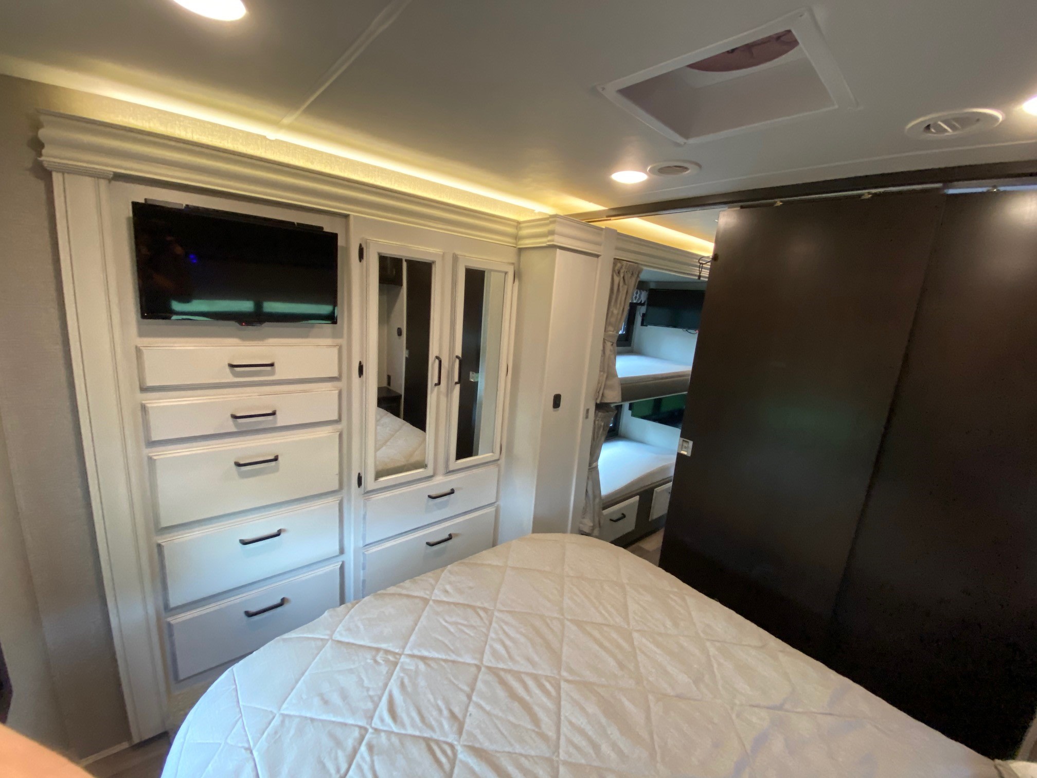Experience comfort in this RV rental bedroom: cozy white bed, integrated dresser, TV, mirrored closet, and bunk beds.. Jayco Greyhawk 2022