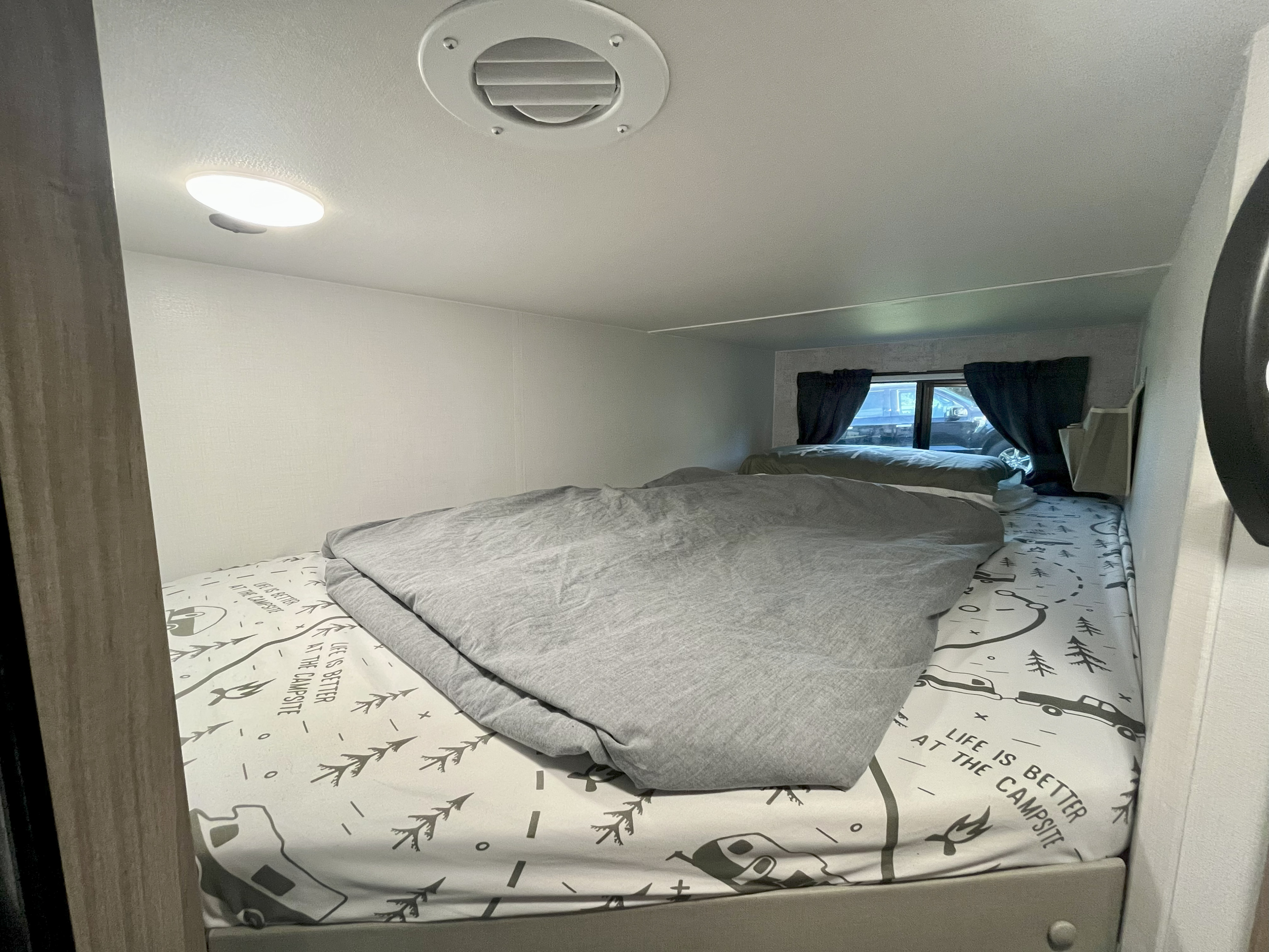 Cozy rv rental bunk beds inside a camper. The beds feature "Life is Better at the Campsite" sheets & a gray blanket.. Winnebago M Series 2025