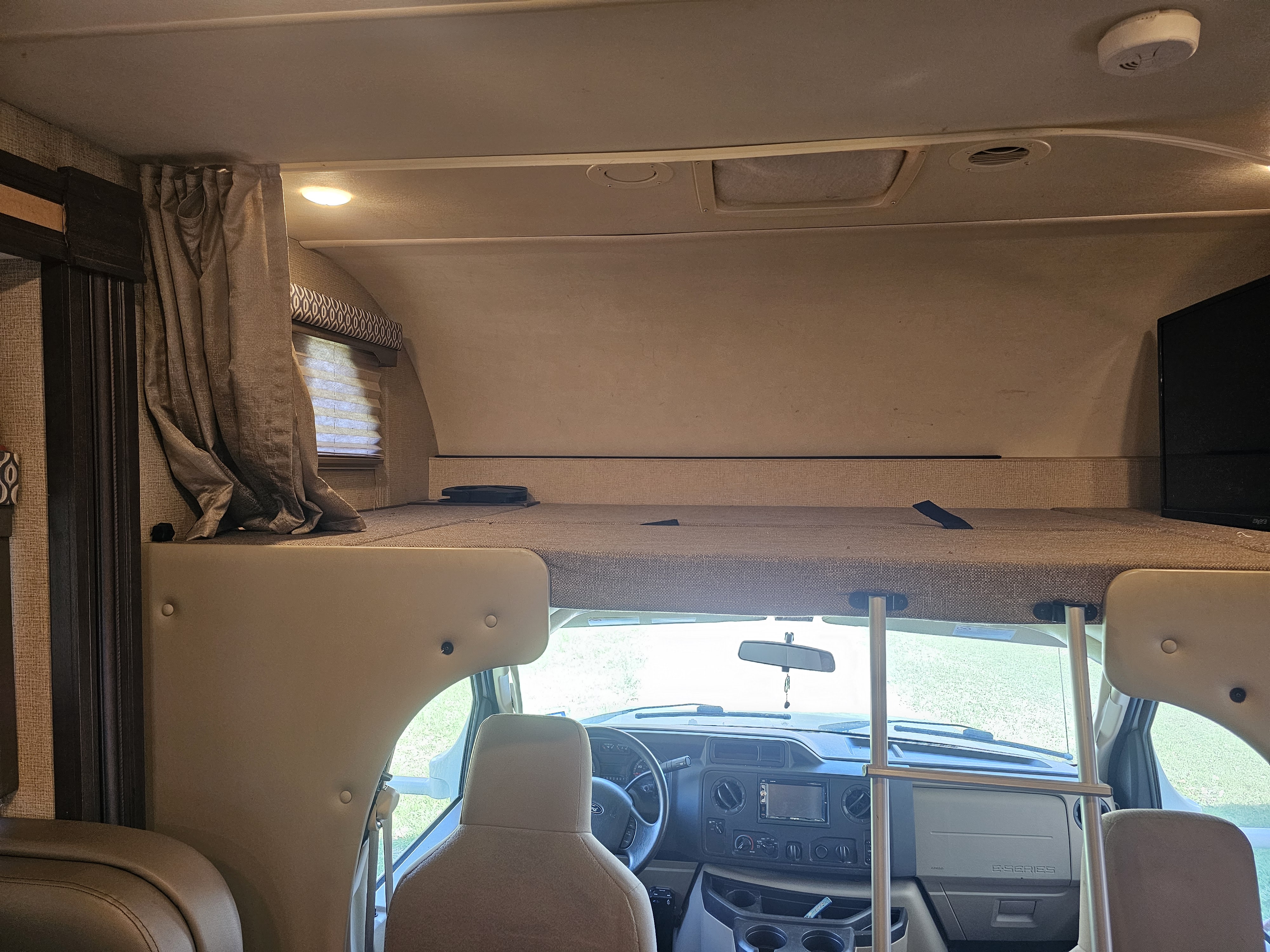Interior of an RV rental, showing the overhead bunk bed, driver's cab area, and a TV on the right.. Thor Freedom Elite 2018