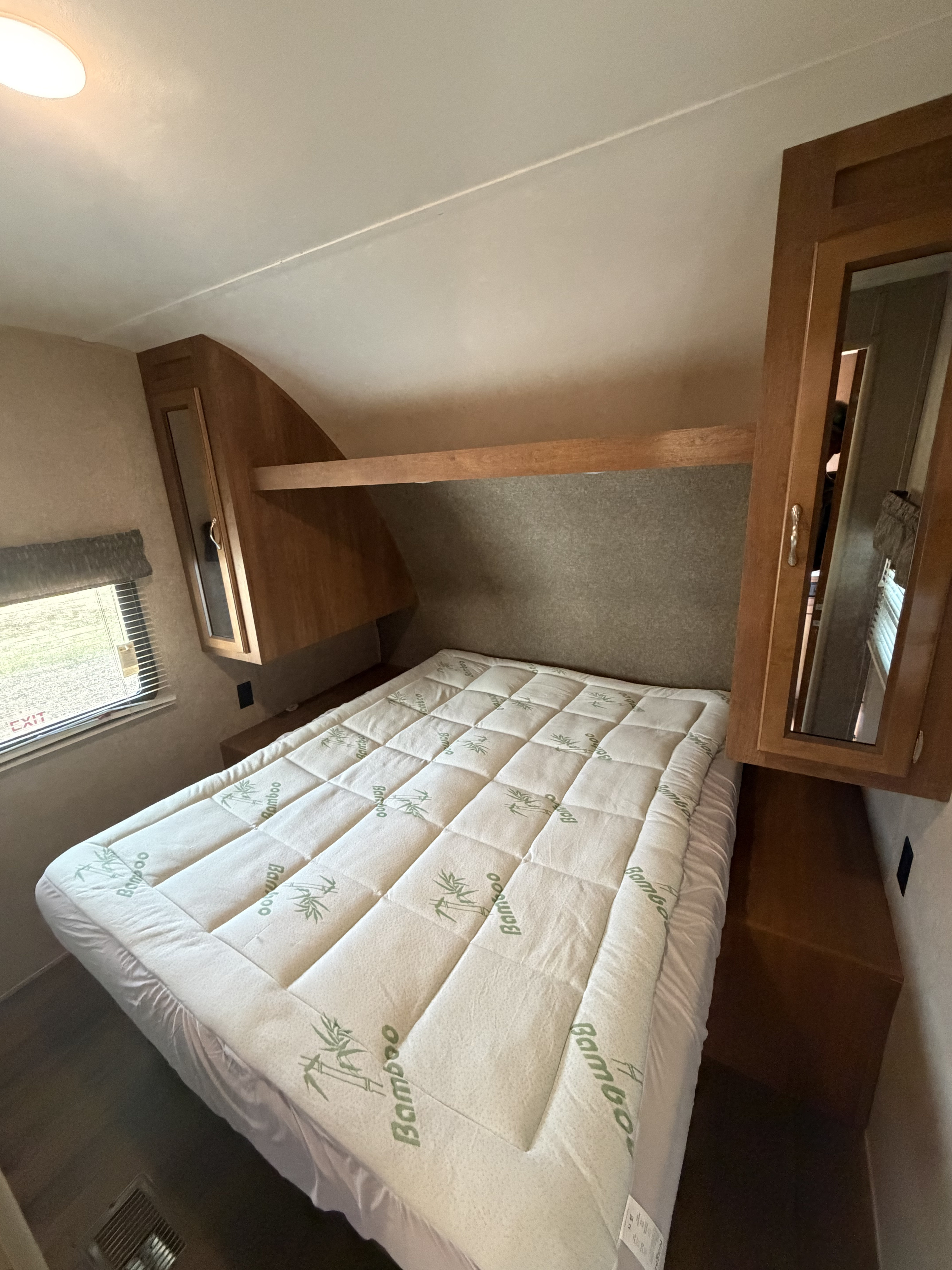 RV rental bedroom featuring a comfortable bed with a bamboo mattress topper, wooden overhead cabinets, and a window.. Coachmen Catalina 261SBH 2018