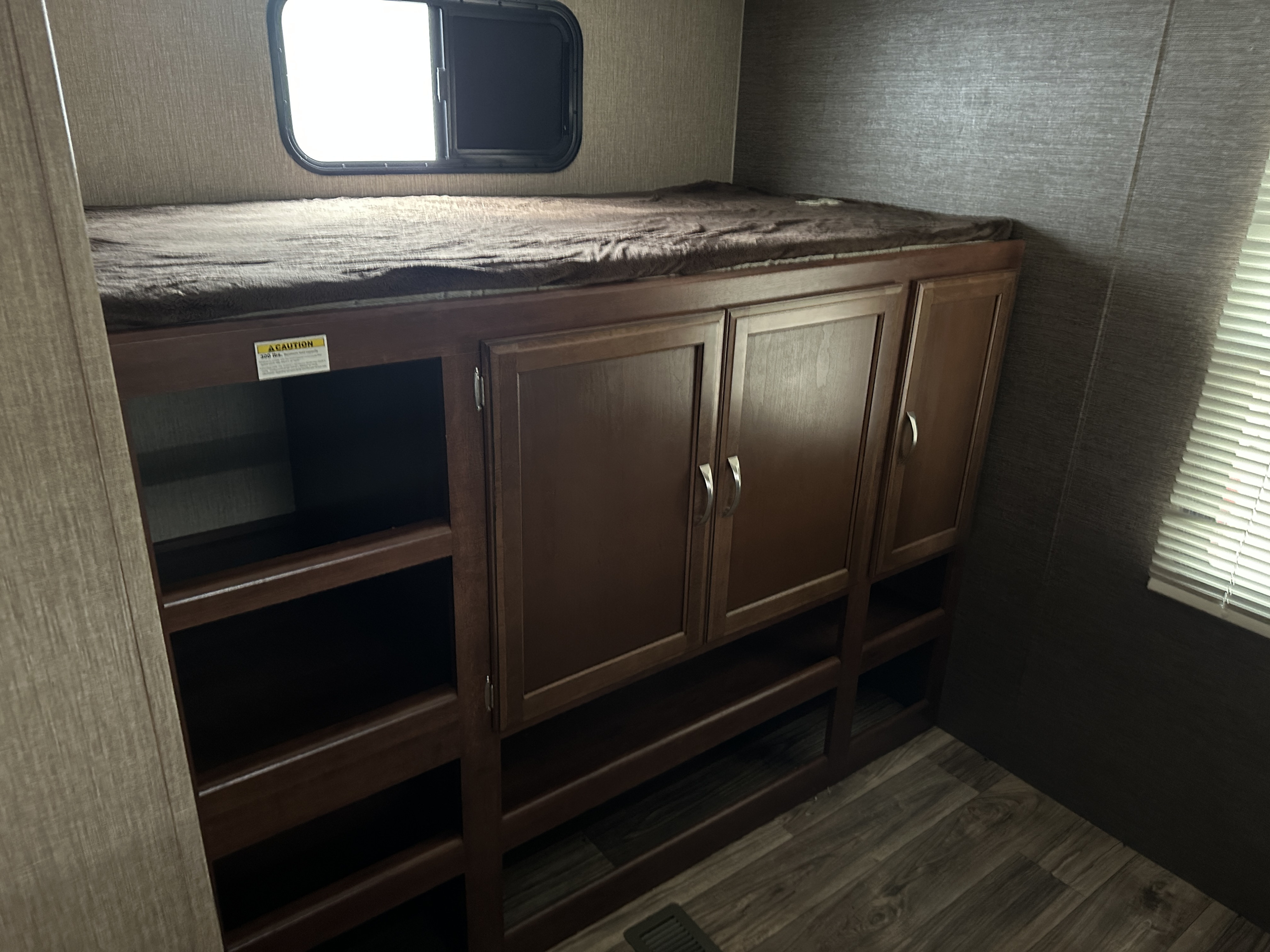 RV rental bunk bed with a window, above built-in dark wood storage cabinets and open shelving for convenience.. Keystone RV Passport Grand Touring 2017