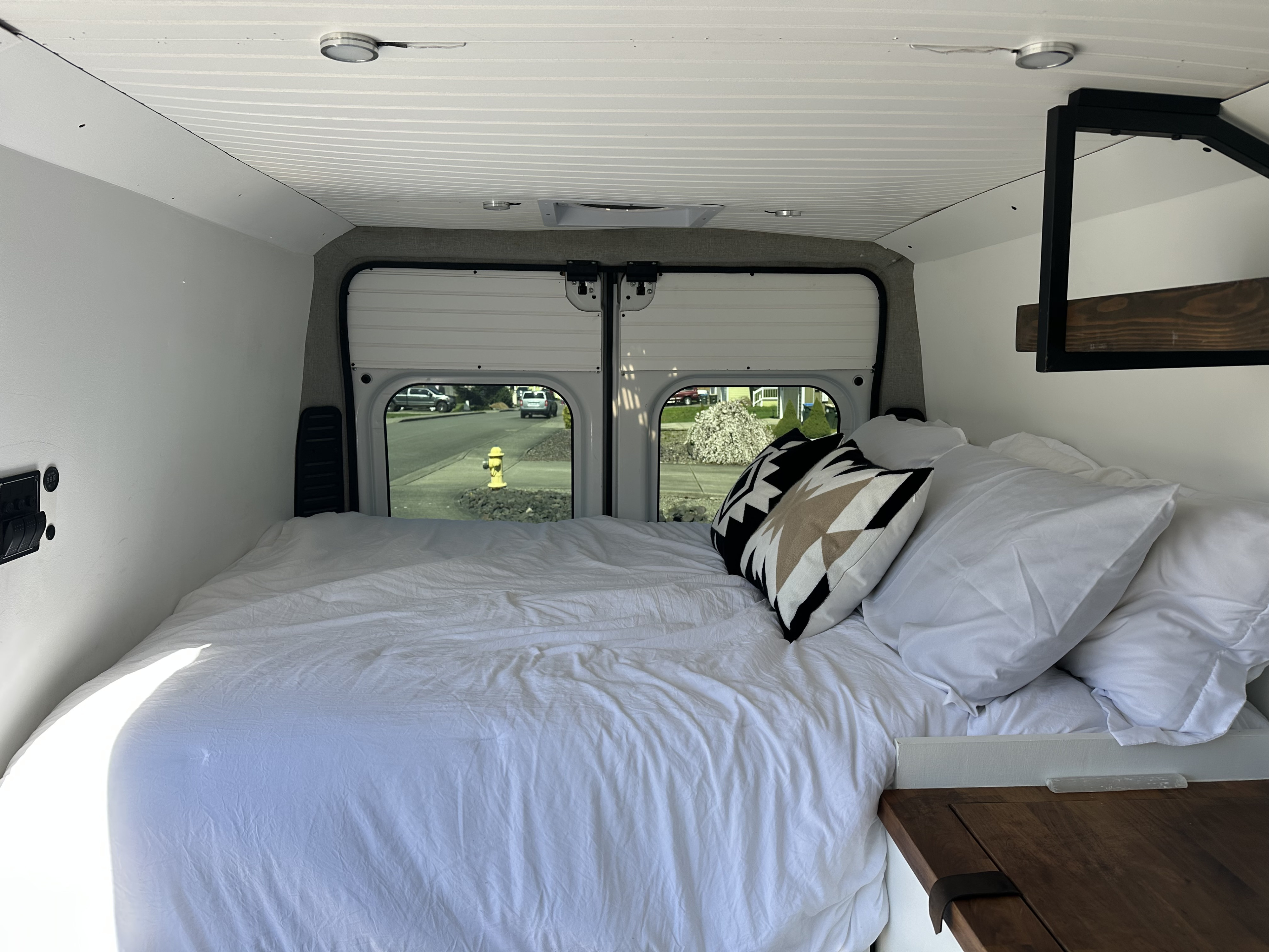 Cozy RV rental bedroom with a large bed, crisp white linens, patterned pillows, and a street view from the rear windows.. Dodge Ram 1500 2016